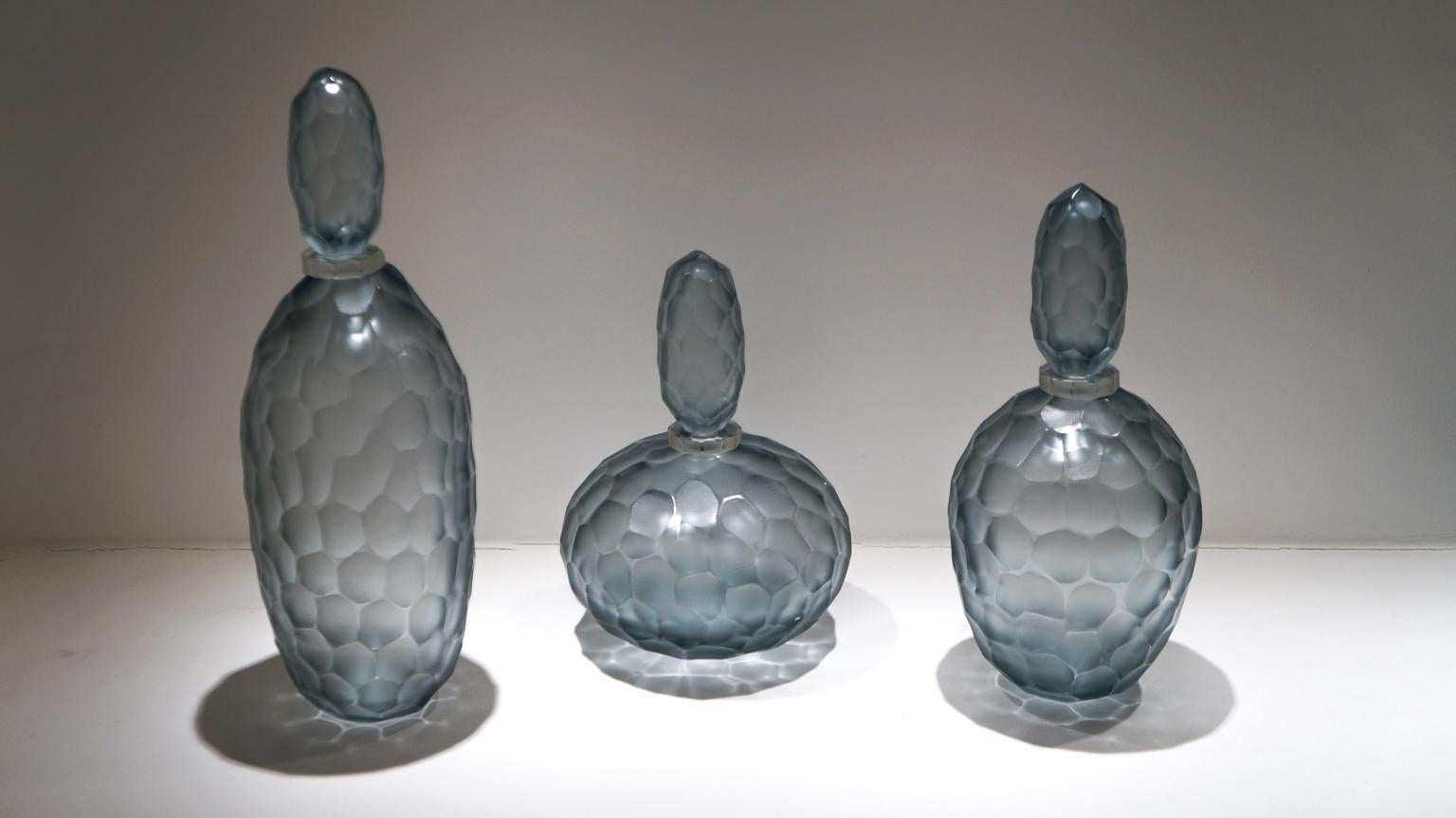 Three bottles engraved entirely by hand with Murano grey blown glass.
To perform this work we need two different processes: the first, to model the hot vase giving form and color. The second, after cooling, it is taken into Moleria where the