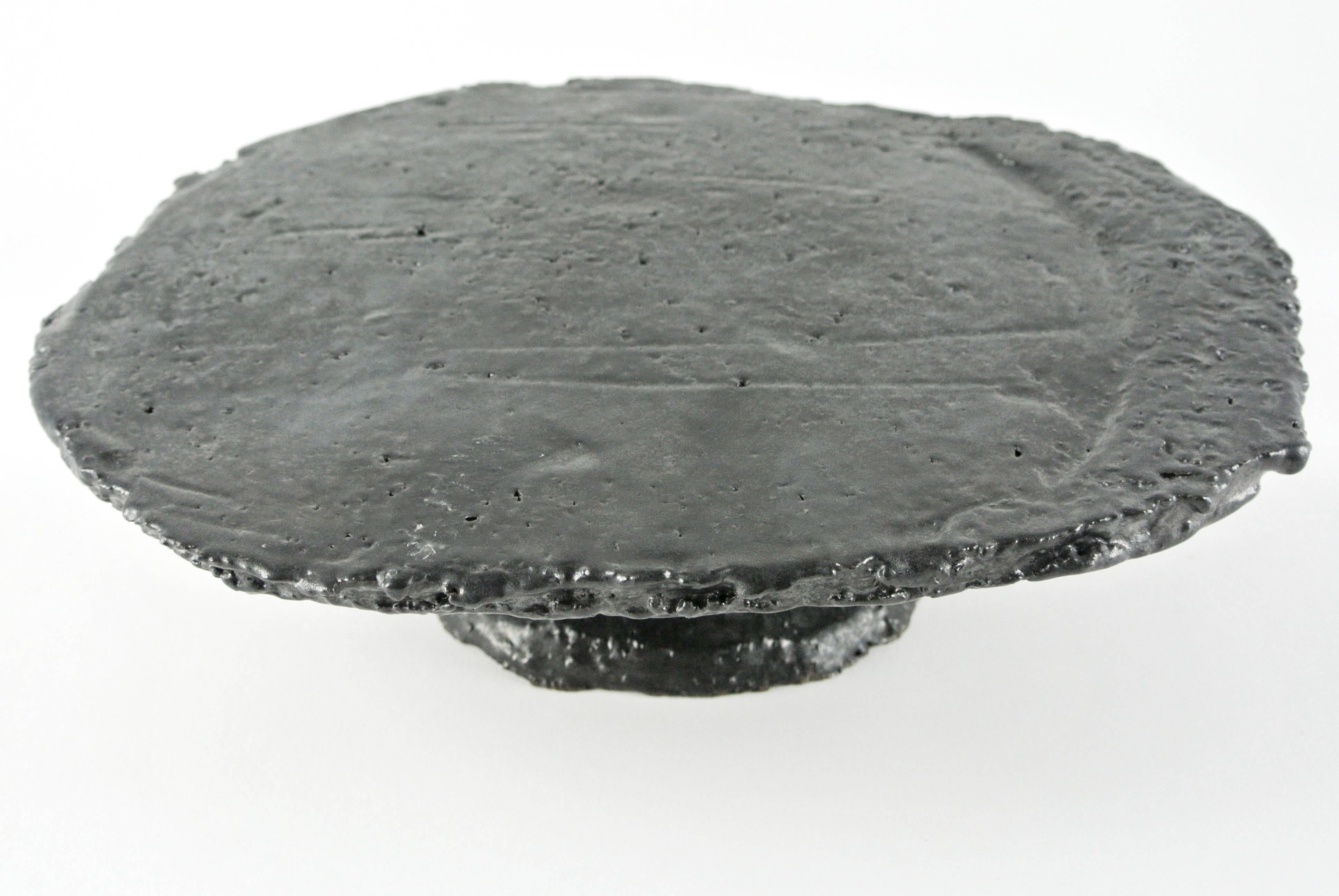 Heavy hand-build platform in rough, grey stoneware. Black glossy glaze with grey nuances. Visible fire sand texture: 24X19X8 cm. Suitable for food.
All pieces by Christine Roland celebrate the imperfections that occur from working with a natural