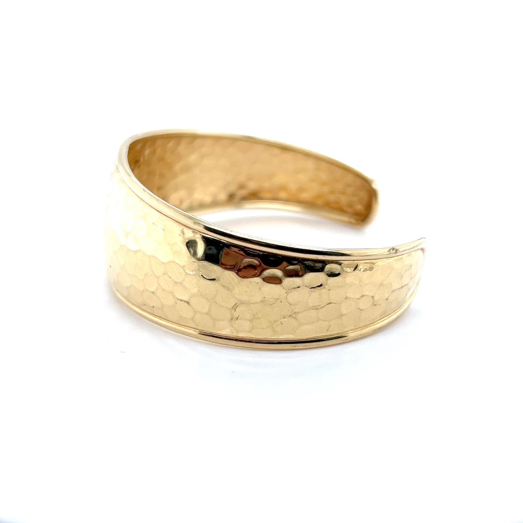 Ce bracelet manchette contemporain est réalisé en or jaune 10 carats et présente une finition martelée qui ajoute de la texture et un éclat subtil à sa surface dorée et chaude. Estampillée 
