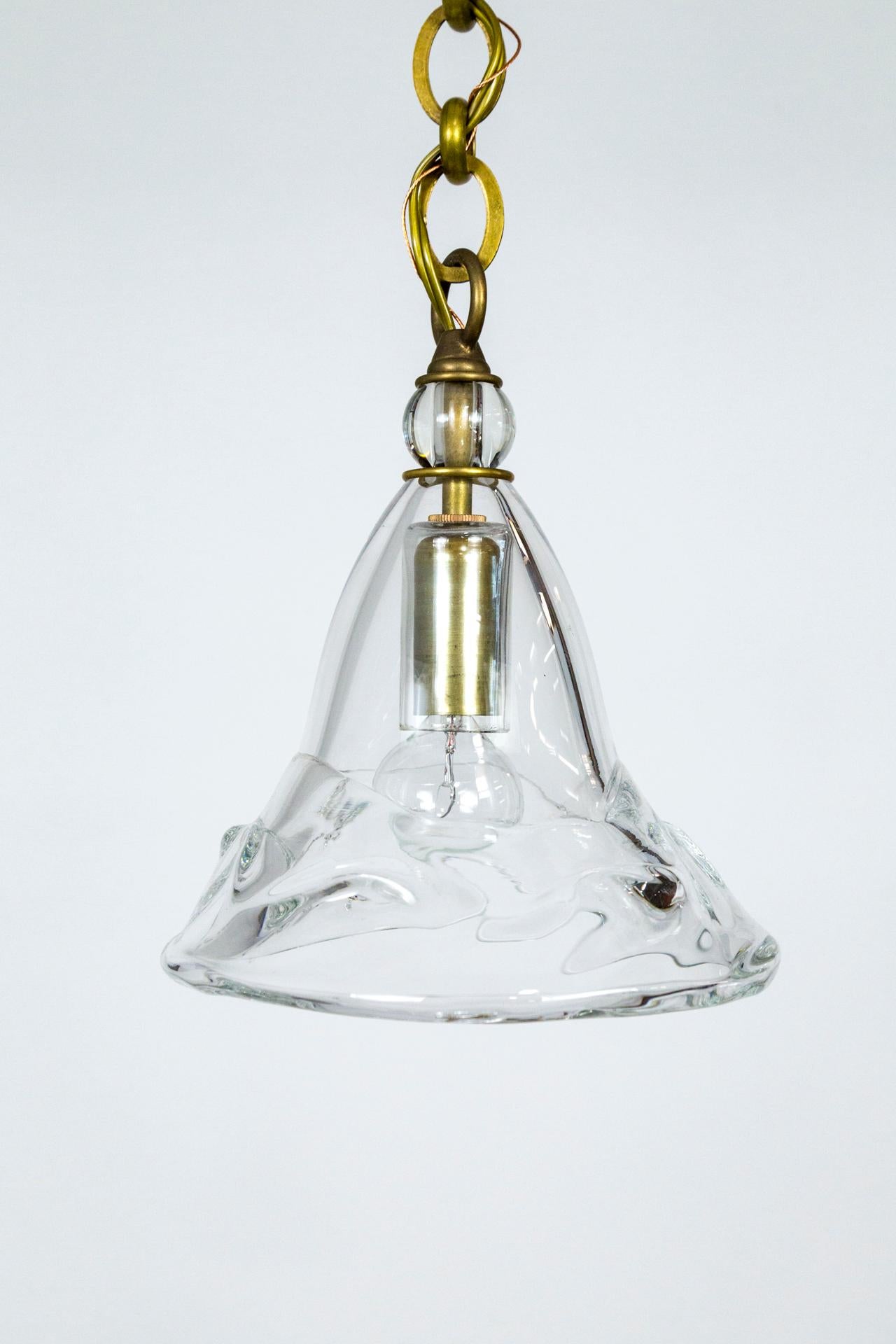A hand blown, irregular, clear glass cone shade topped with a large crystal bead, finished with a sleek, chunky brass chain and canopy. A candelabra size, brass socket with a glass cap. Measures: 8