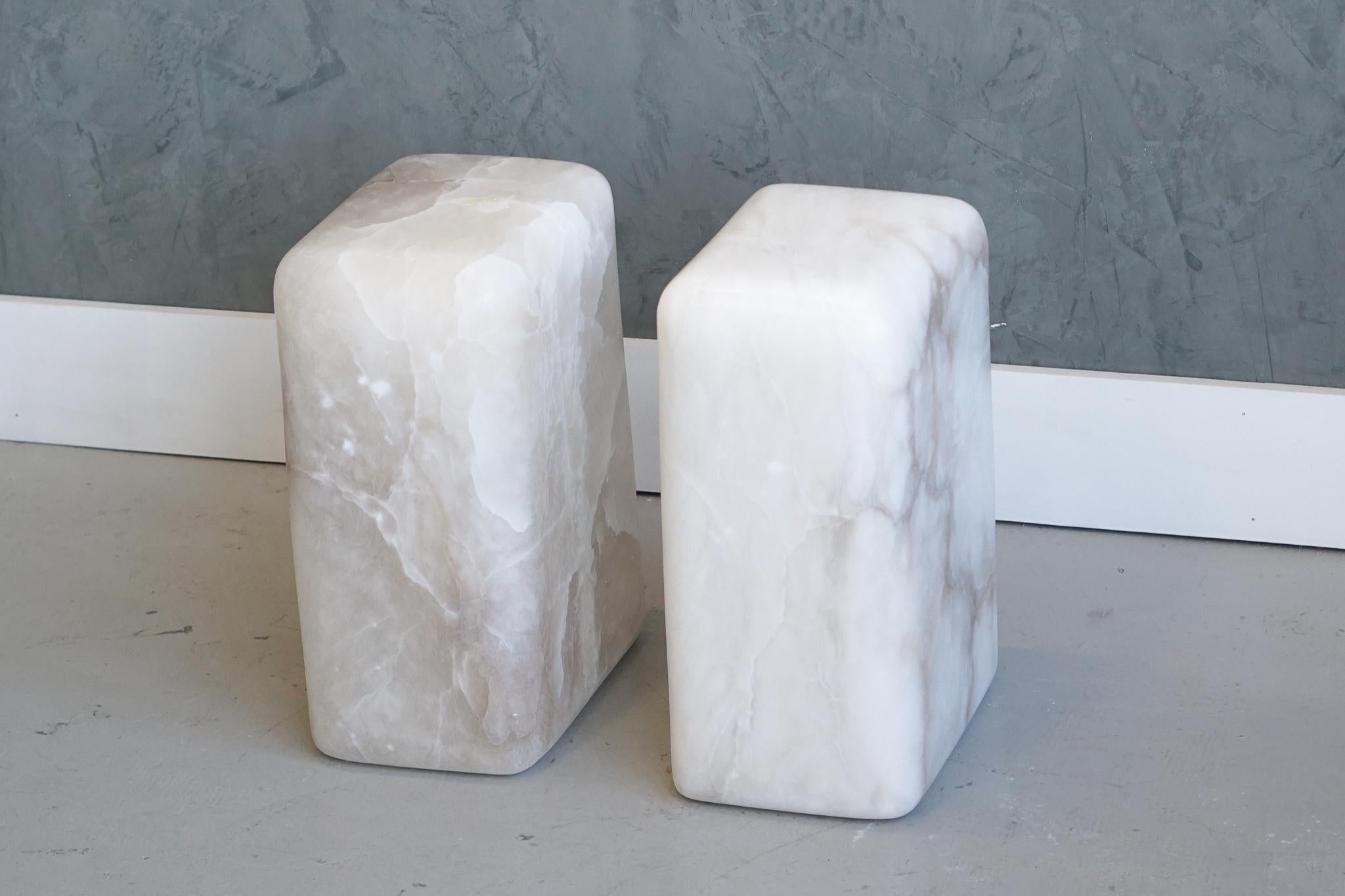 These side or end tables have been hand shaped from a solid block of white alabaster. The unique coloration and veining in the blocks are the focal point of this simple yet captivating piece. 

Alabaster color / veining will vary from piece to