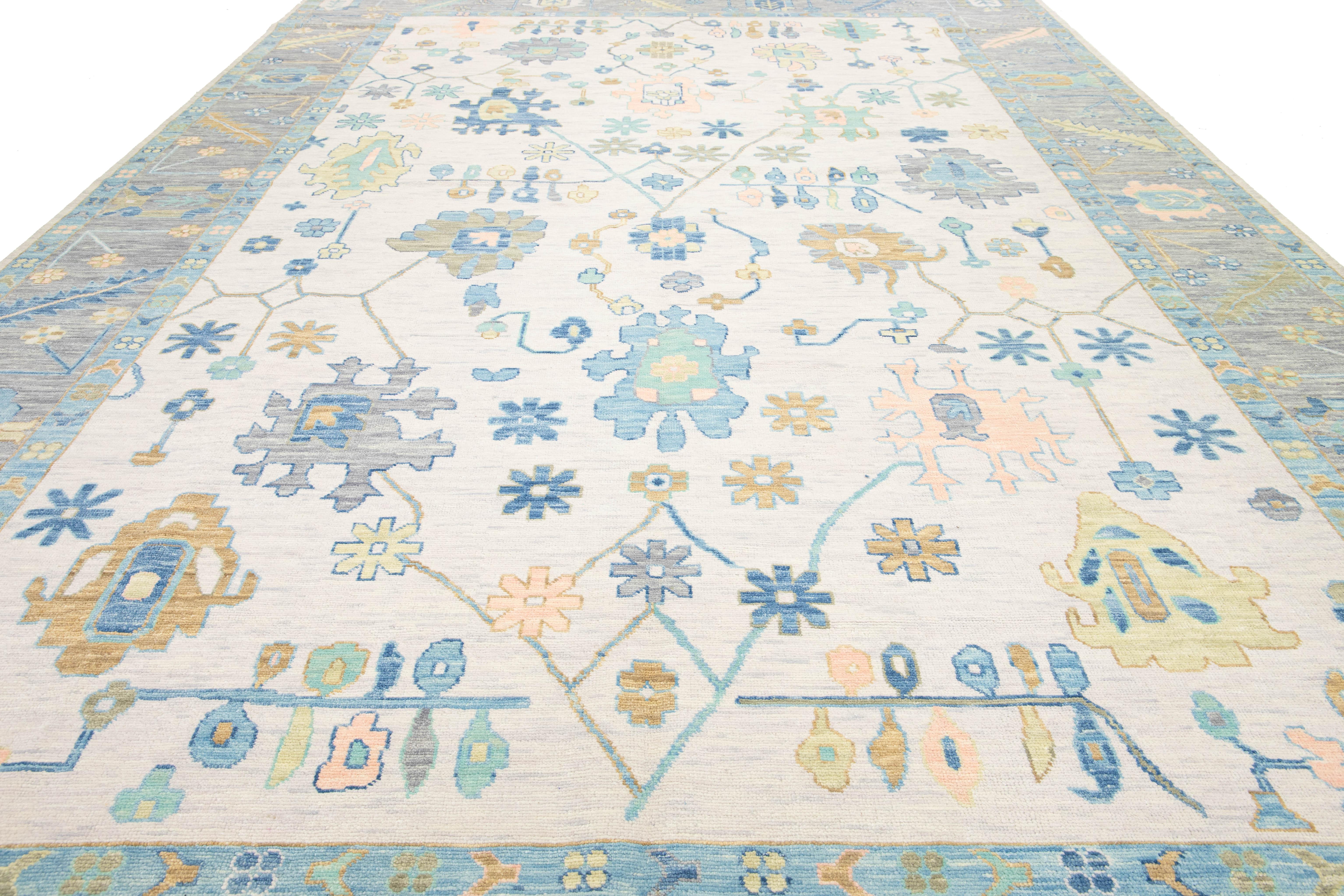 This Modern Oushak Style Wool Rug combines a contemporary flair with traditional Oushak artistry. It showcases a soft beige background adorned with vibrant floral patterns in shades of blue, brown, and gold, gracefully spreading across the rug. This