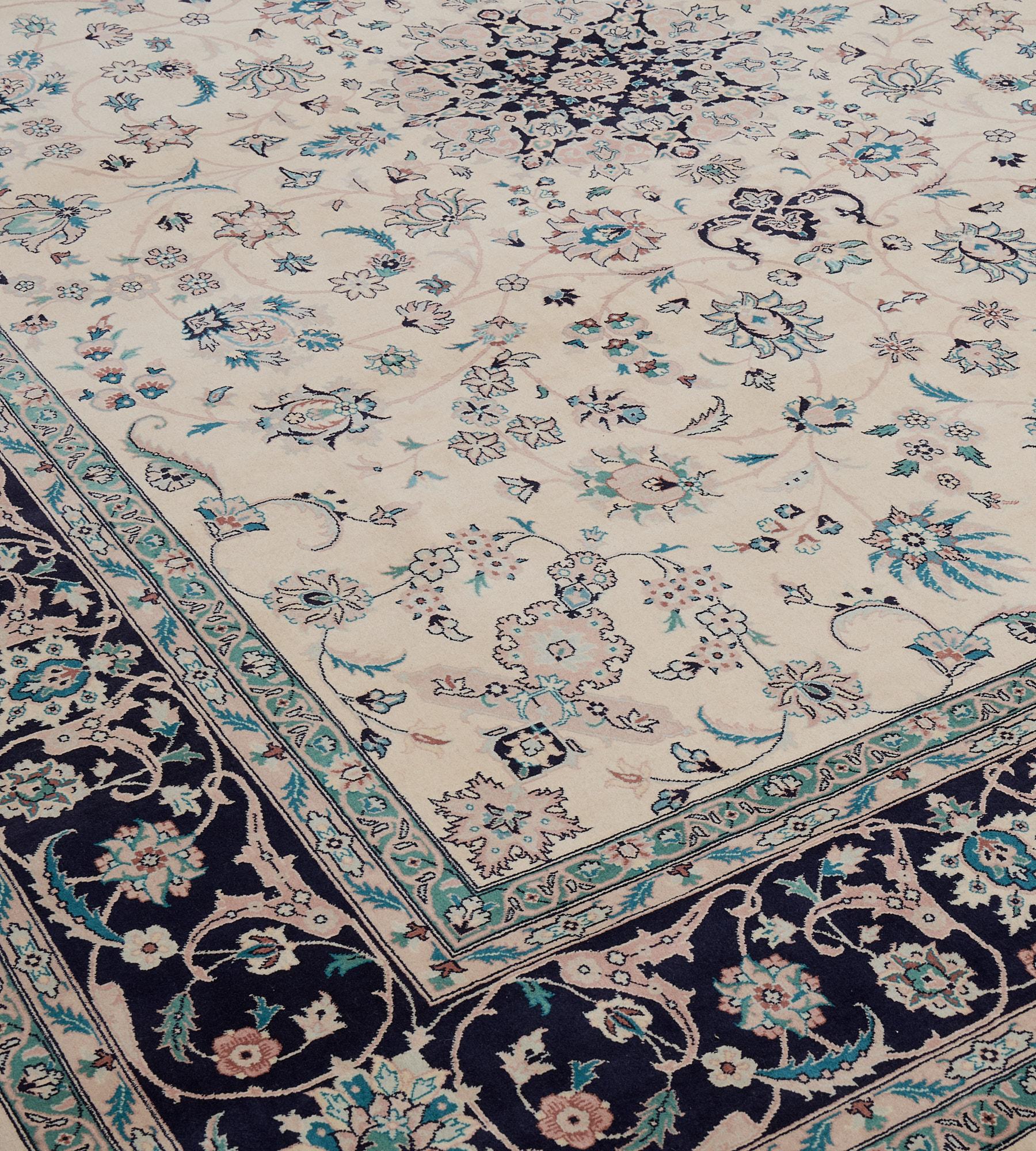 This revival Tabriz has an ivory central field with a center polychrome palmette surrounded by a delicate polychrome flowerhead vine in a deep navy border of polychrome turtle-palmette vine border between narrow floral ivy stripes. 