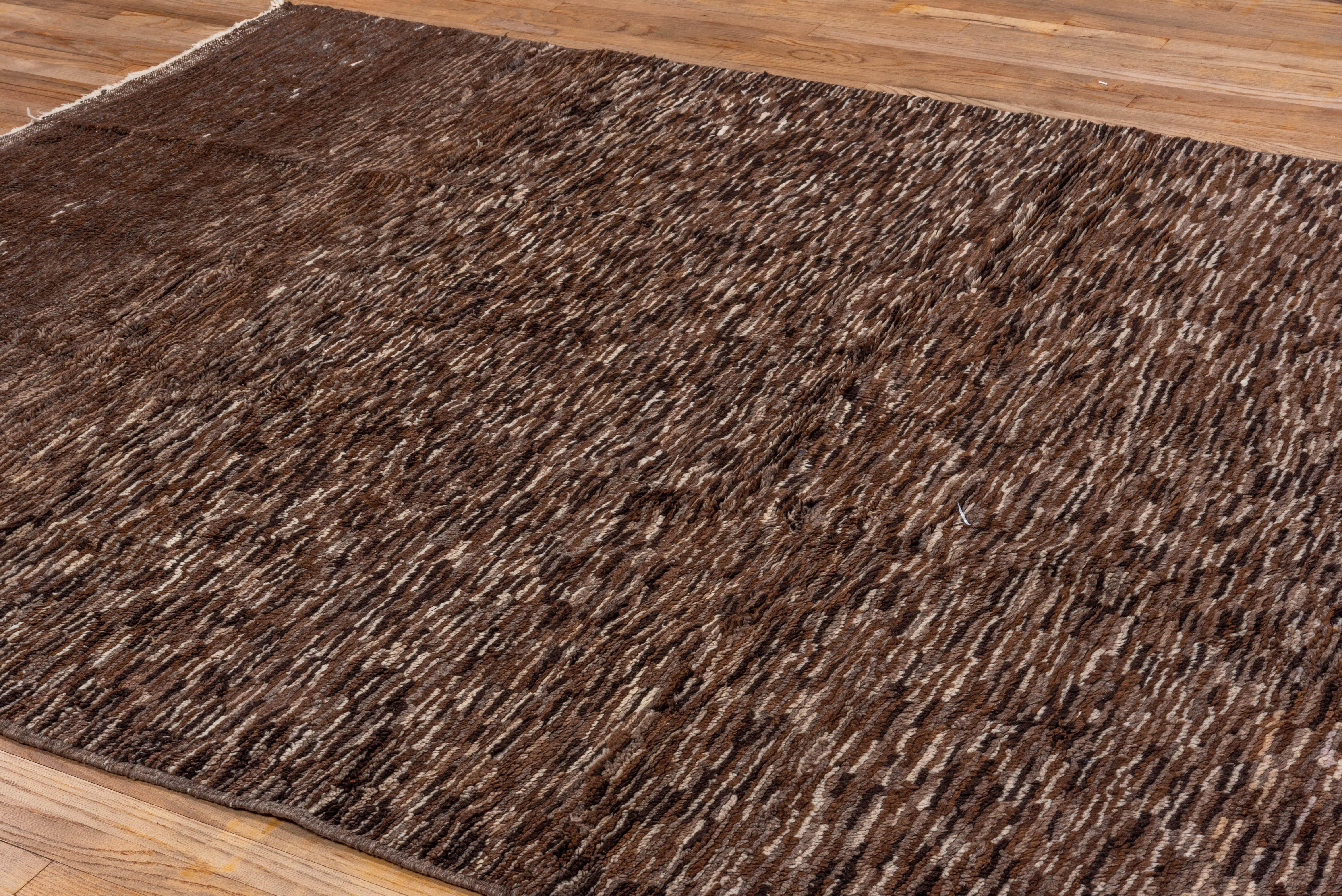 This contemporary hand-knotted rug features a dense, speckled weave in layered shades of mocha, walnut, and taupe. Its subtle tonal movement and soft texture offer a grounded, organic presence ideal for minimalist and modern interiors.