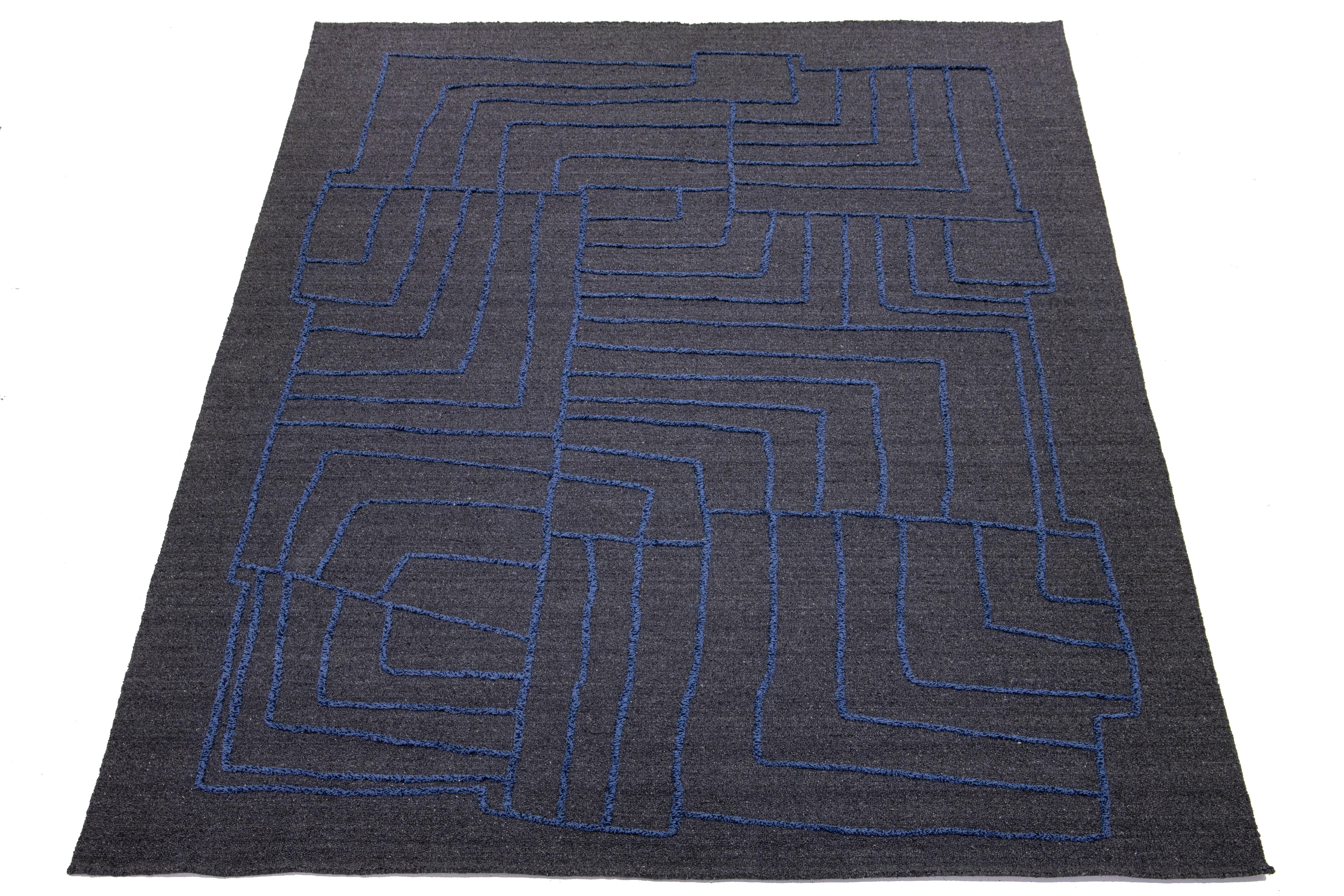 This exquisitely designed modern wool rug is bound to captivate attention. Its sophisticated gray background provides the perfect canvas for the intricate abstract pattern in blue hues. This striking visual contrast infuses depth and personality