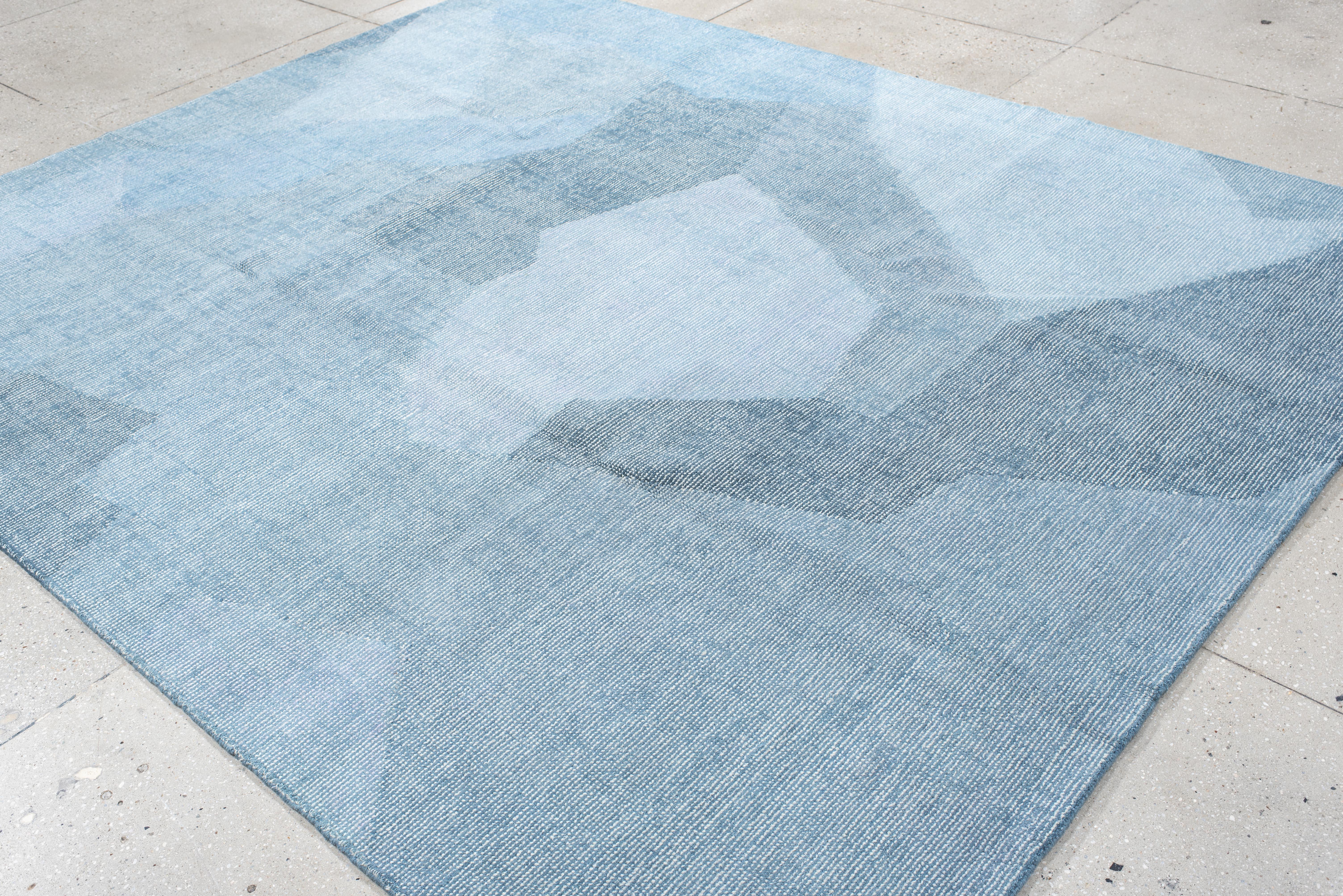Esta alfombra contemporánea tejida a mano presenta un sofisticado diseño geométrico abstracto, caracterizado por formas angulares en capas en un relajante degradado de tonos azul hielo, pizarra y gris acero. La composición minimalista evoca una
