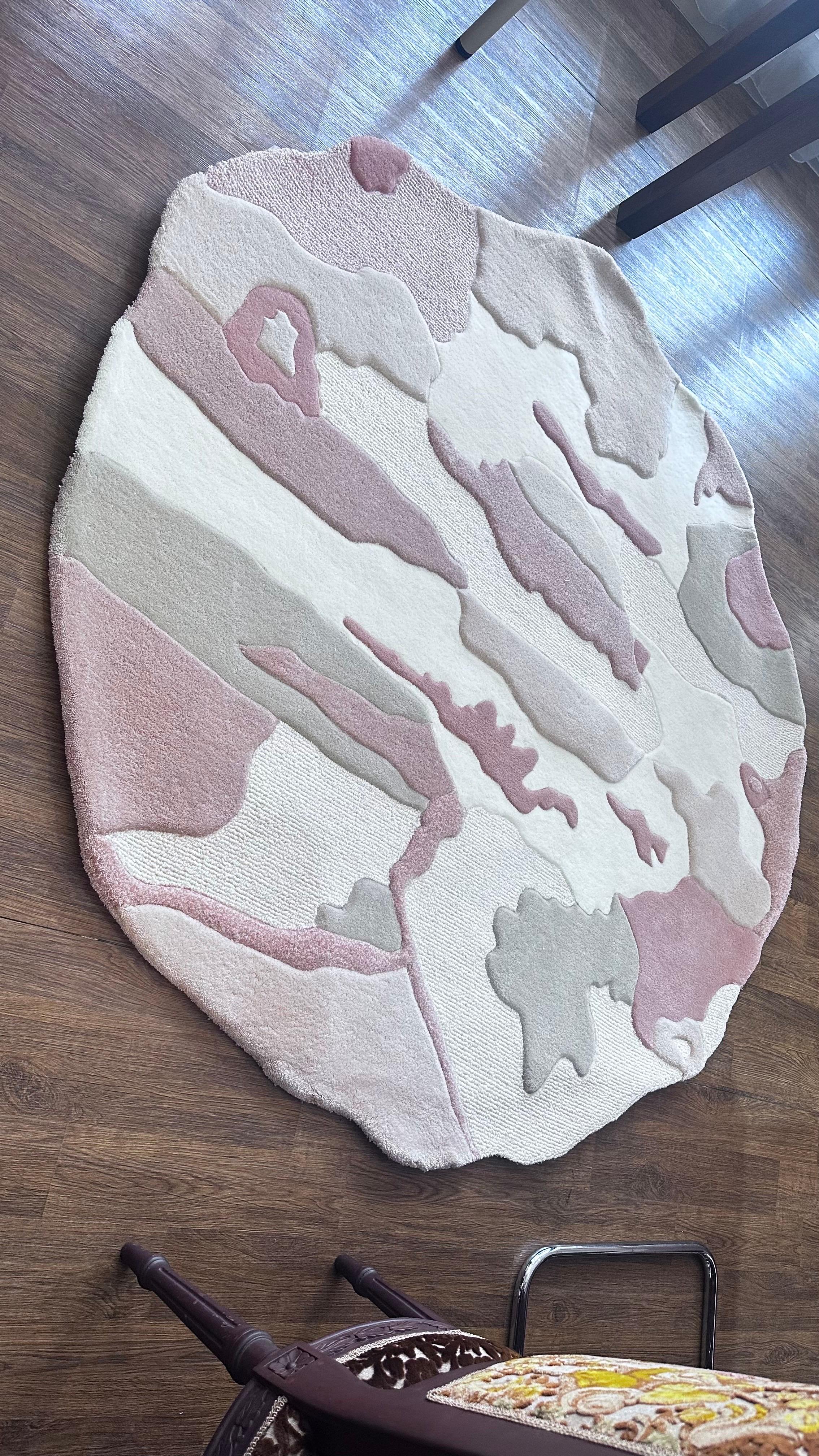This contemporary hand-tufted wool rug is a unique statement piece, defined by its organic round silhouette and abstract painterly design in blush, beige, cream, and muted terracotta. The flowing composition evokes the softness of natural