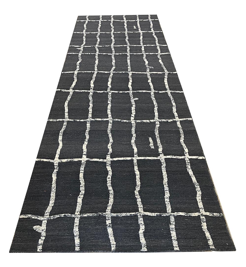 Tappeto dal design moderno annodato a mano in lana organica, nei toni del grigio molto scuro, del carbone e del crema, caratterizzato da un disegno di linee leggermente storte che attraversano la lunghezza del campo.

Questo splendido tappeto a