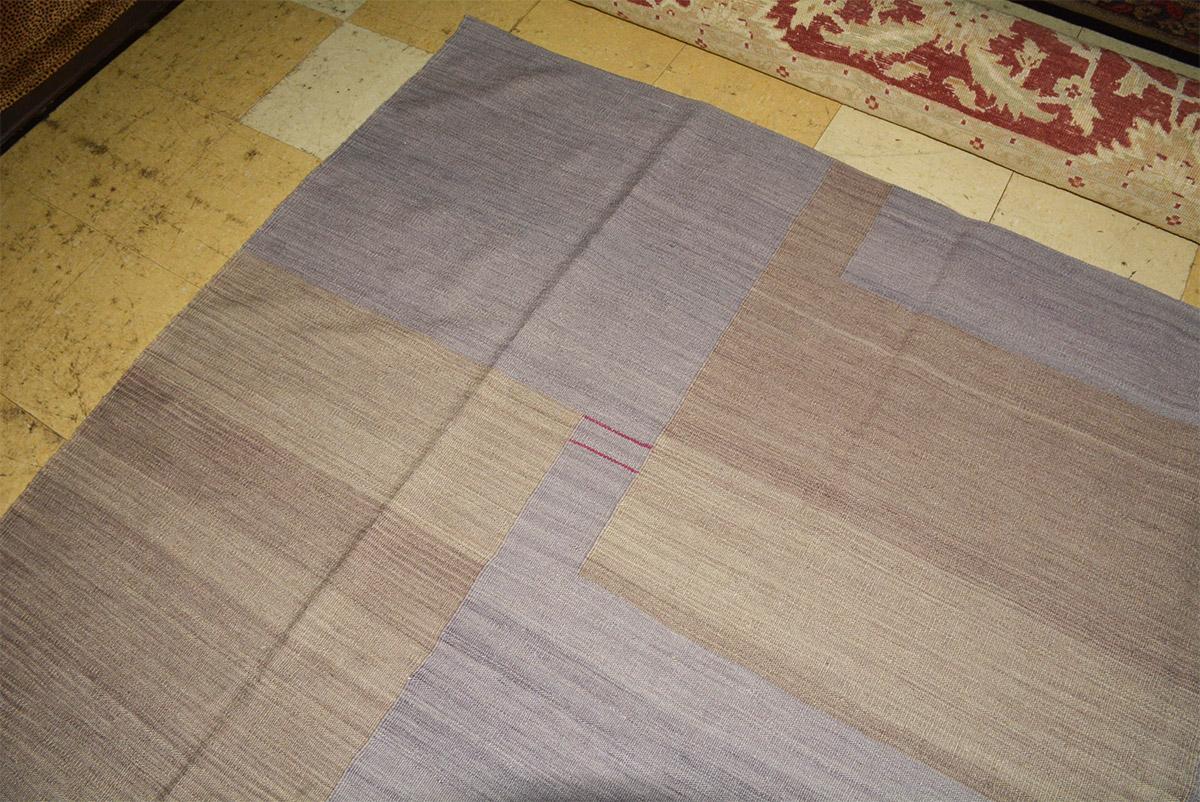 The contemporary Kilim rug was 100% handwoven in Pakistan. The pattern has the effect of patchwork in shades of tans and lavender. Varying red stripes add contrast. 90% wool and 10% polyester in a flat-weave. The ends are tape bound underneath. Dry