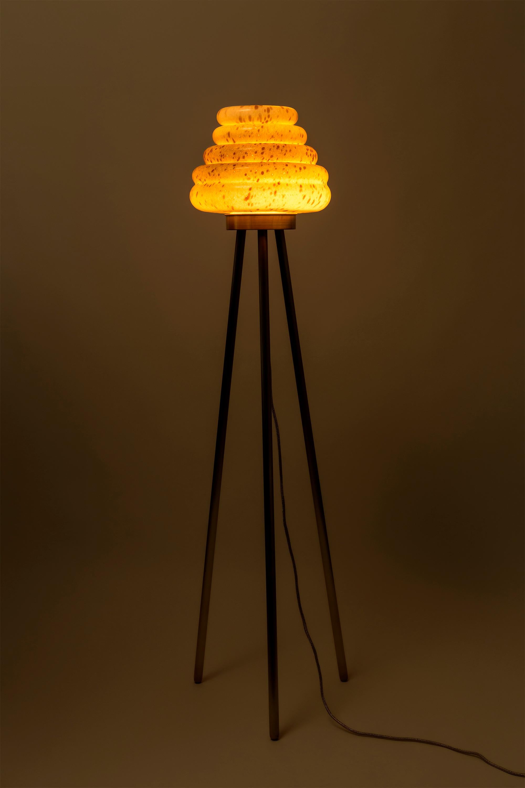 This beehive inspired floor lamp comprises a mixed colored hand-blown glass shade and different combinations of wood veneer legs and copper. Second version of Colmena has the dotted patterned glass shade and matte brass legs. The light is adjustable