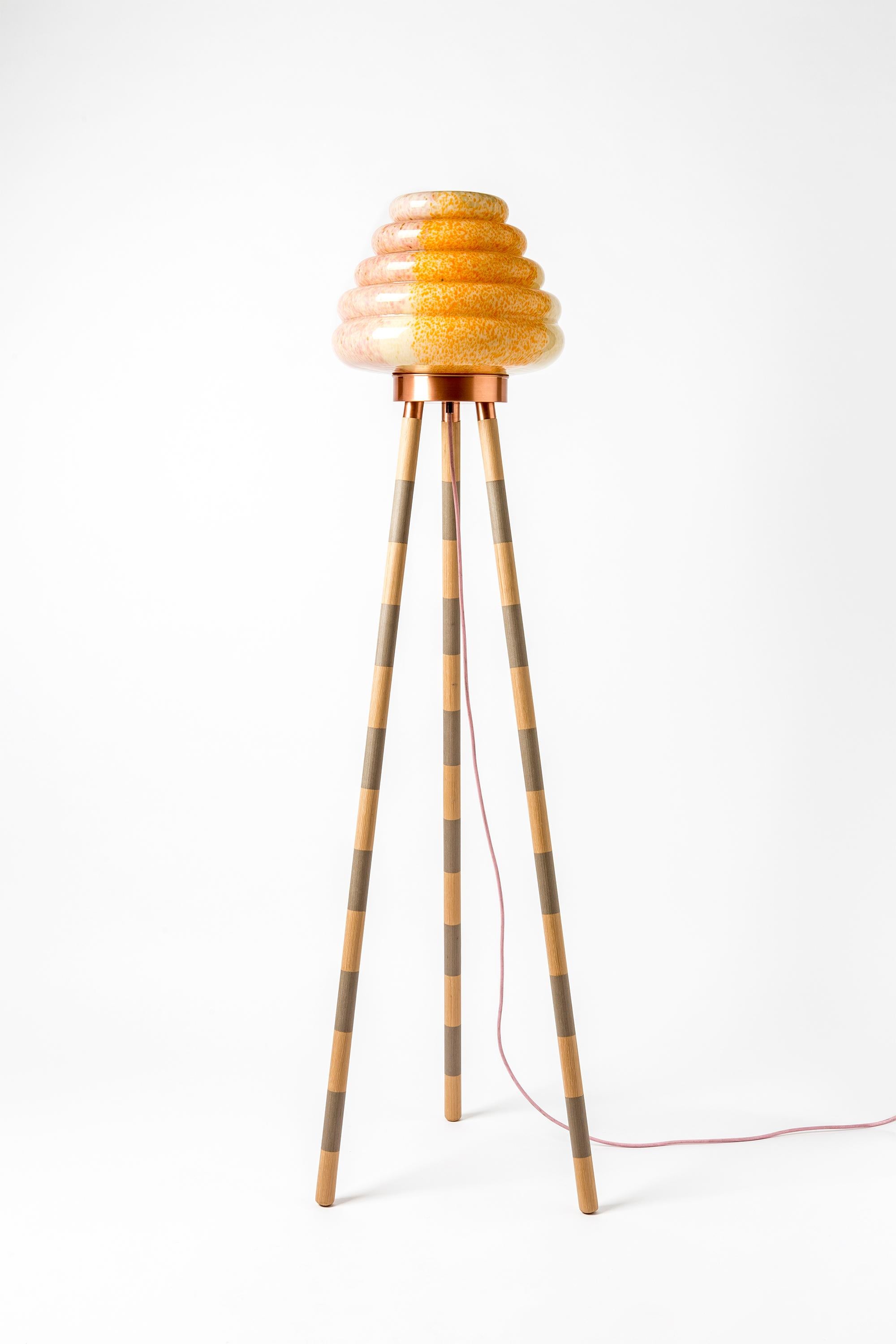 This beehive inspired floor lamp comprises a mixed colored handblown glass shade and different combinations of wood veneer legs and copper. The light is adjustable by the dimmer. Each piece is unique and custom-made.