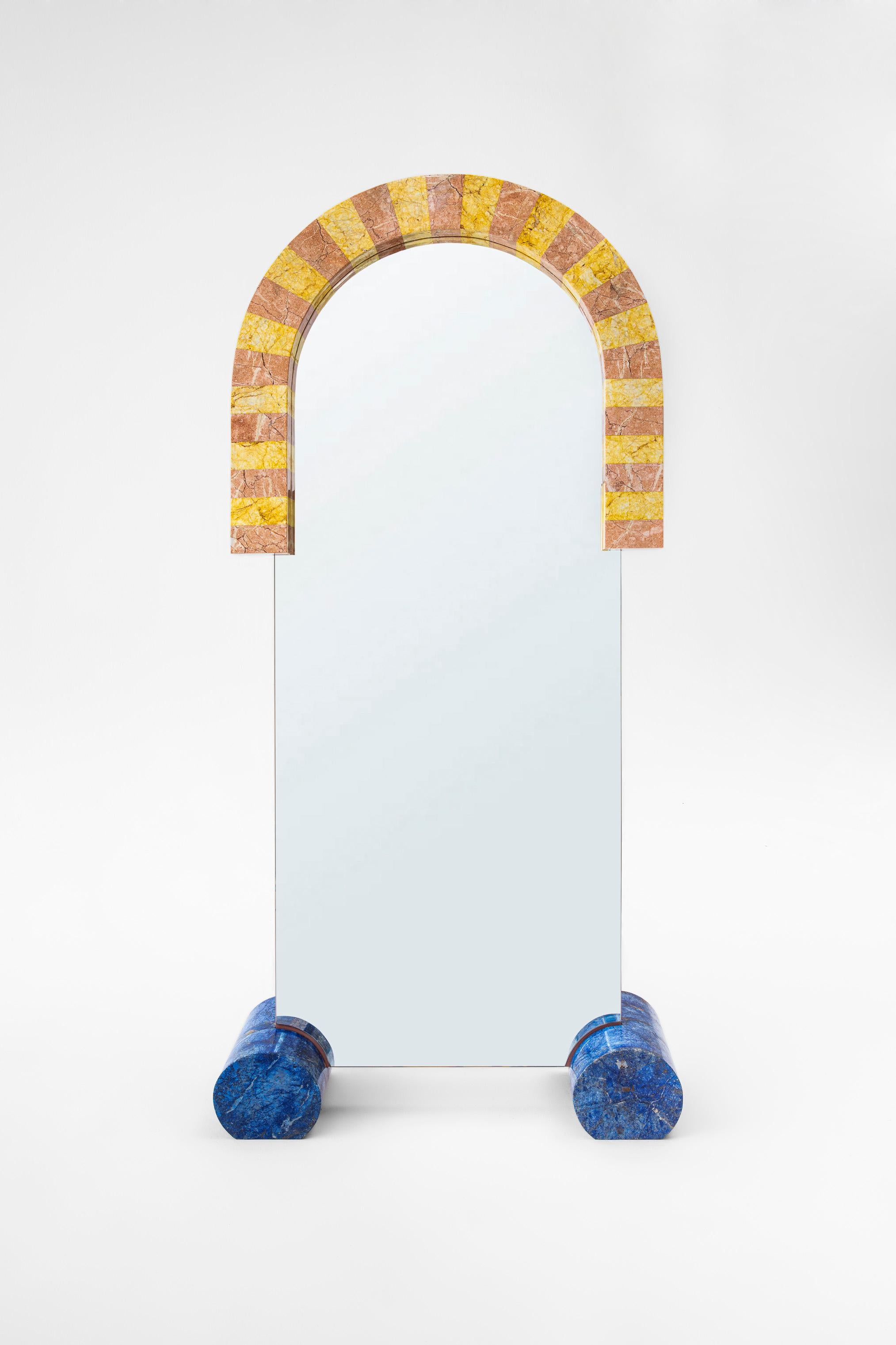 “Zaziko Mirror” resembles a giant colorful toy made out of marble. Zaziko is handcrafted and assembled with pink and yellow marbles creating a semi arch shape around the clear mirror. 2 giant cylindrical blue painted marble pieces allows support on