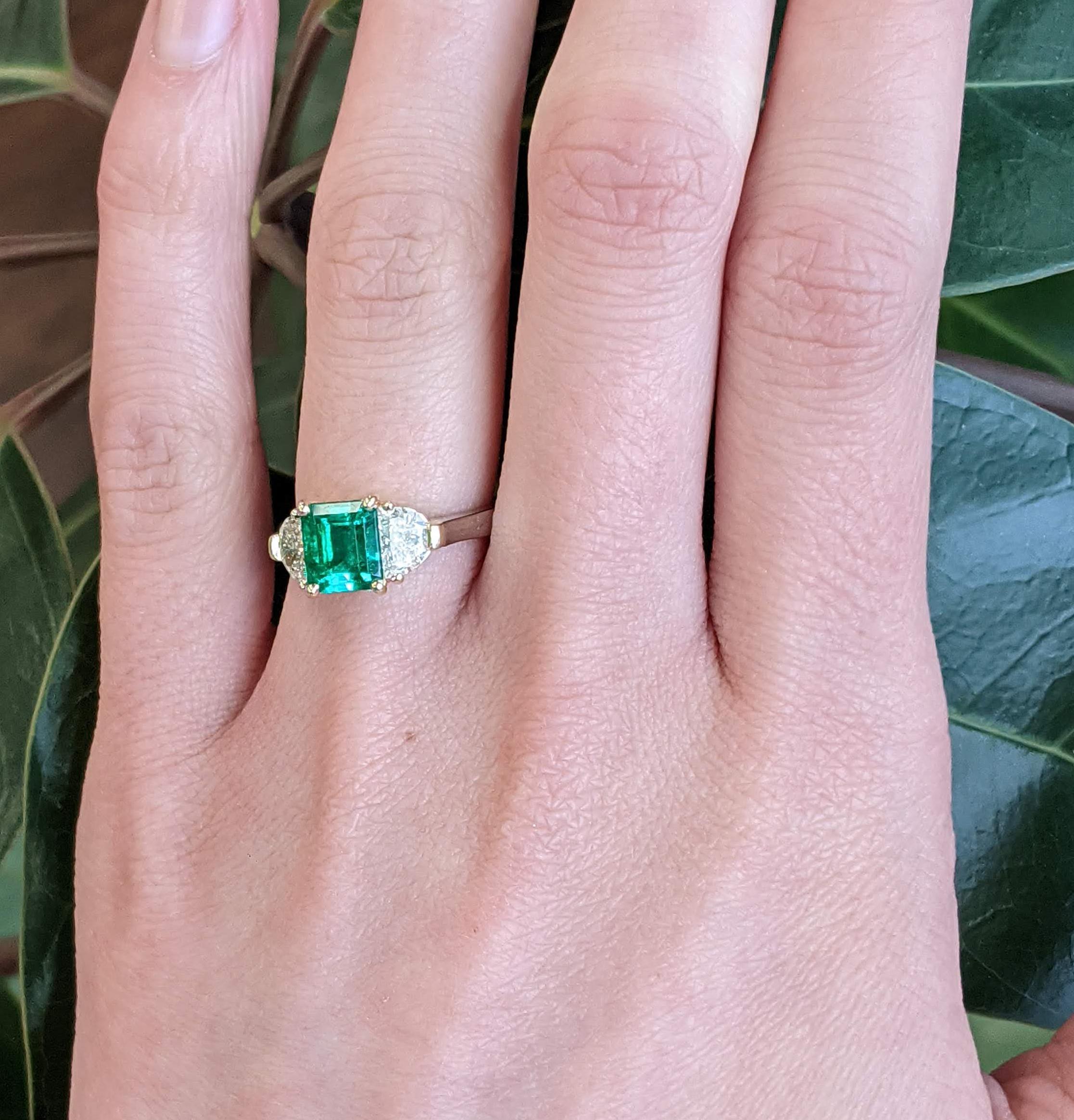 This breathtaking ring is in 18k yellow gold and platinum, boasting a killer deep green emerald center stone flanked by two perfectly matched brilliant white half-moon diamonds. The emerald center is a stunning deep green color and an elegant square