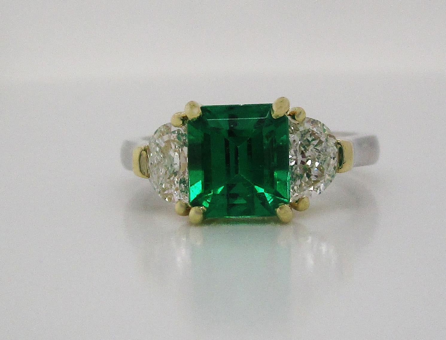This breathtaking ring is in 18k yellow gold and platinum, boasting a killer deep green emerald center stone flanked by two perfectly matched brilliant white half-moon diamonds. The emerald center is a stunning deep green color and an elegant square