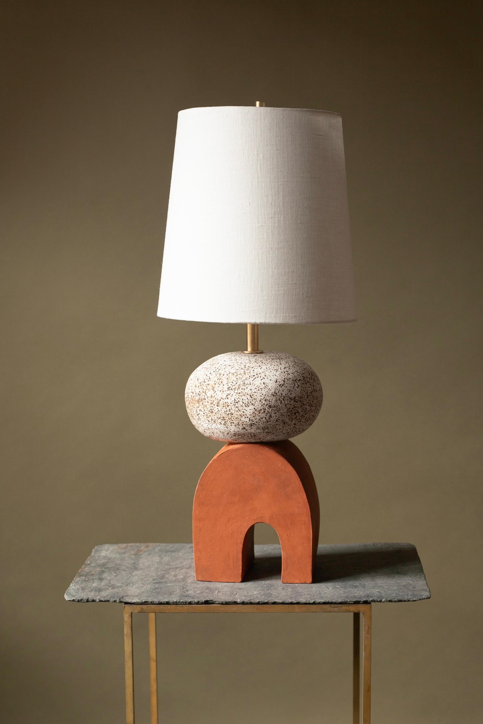 Einzigartige Lampe, auf der Drehscheibe gedreht und mit rotem und gesprenkeltem Steinzeugton handgefertigt. Etwa 22 Zoll hoch, mit Leinenschirm, unbearbeiteten Messingbeschlägen und einer blauen geflochtenen Kordel.

Versandfertig in 6-10