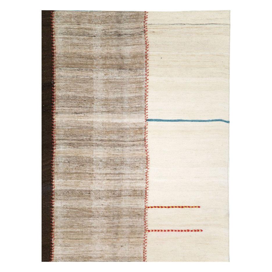 Un tapis d'accent contemporain tribal persan Kilim à tissage plat, fait à la main au cours du 21e siècle, avec 5 colonnes dans des tons neutres de crème et de brun, cousues ensemble en rouge et avec quelques lignes bleues abstraites.

Mesures : 6'