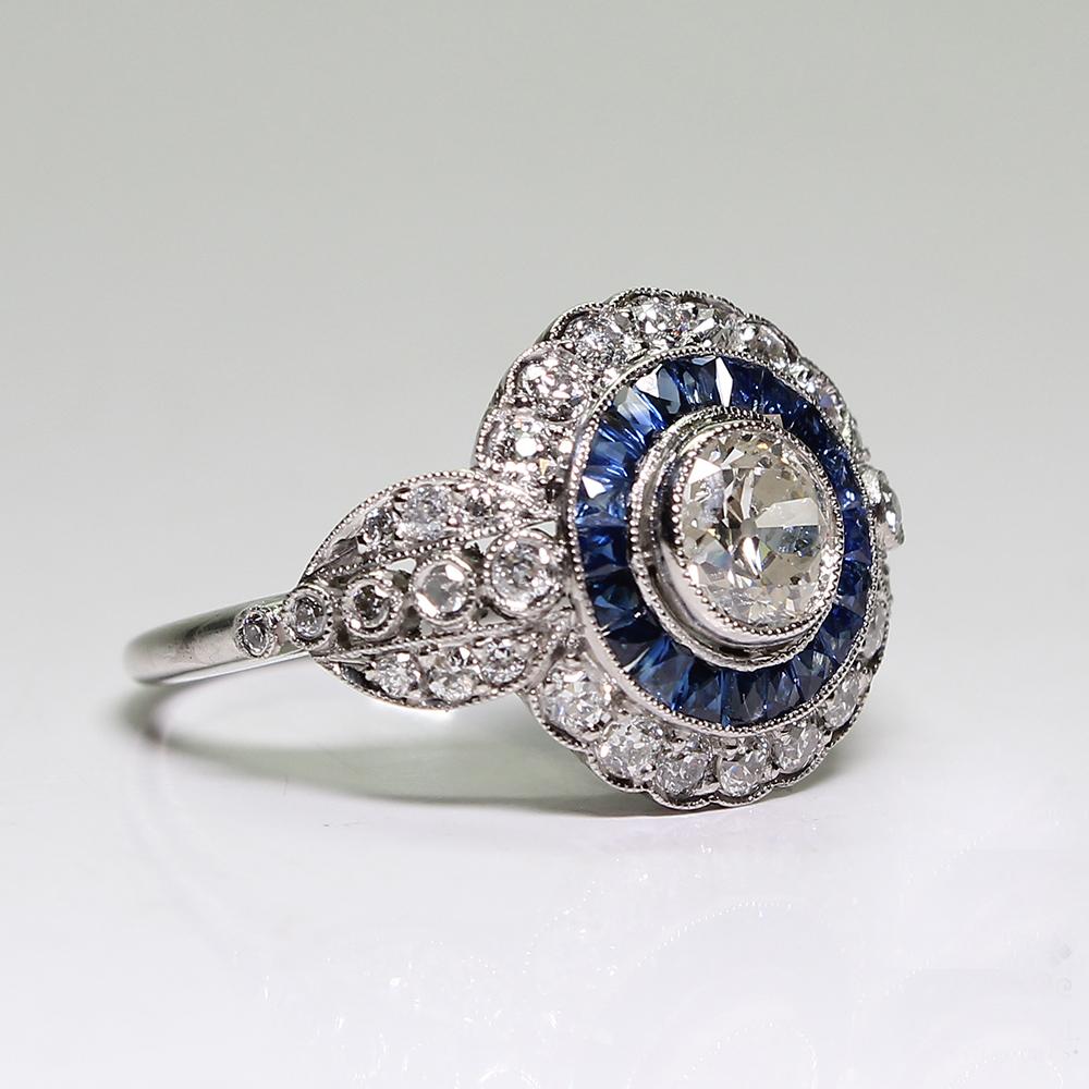 Composition: Platinum

Stones:
•	1 Old mine cut diamond of H-VS2 quality that weighs 1ctw. 
•	36 Old mine cut diamonds of G-VS2 quality that weigh 0.80ctw. 
•	20 natural calibrated French cut sapphires that weigh 0.90ctw.
Ring size: 6 ½ 
Ring face: 
