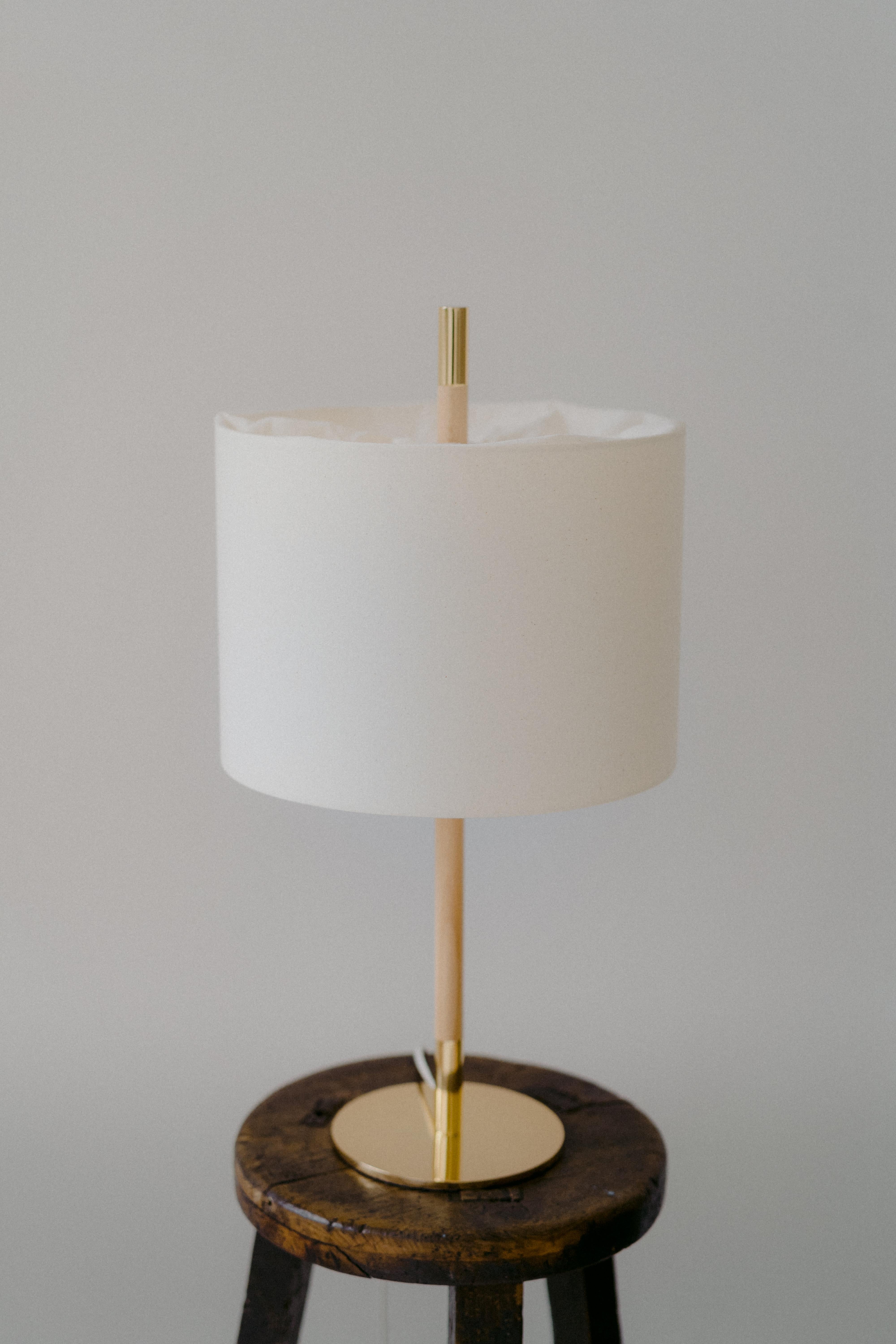 AMÀ TABLE LAMP

The Amà lamp model offers a variant with a natural textured fabric shade in white.
At the top, the fabric folds to hide the light source, creating a unique detail.
As in the rattan version, its foot combines polished brass with