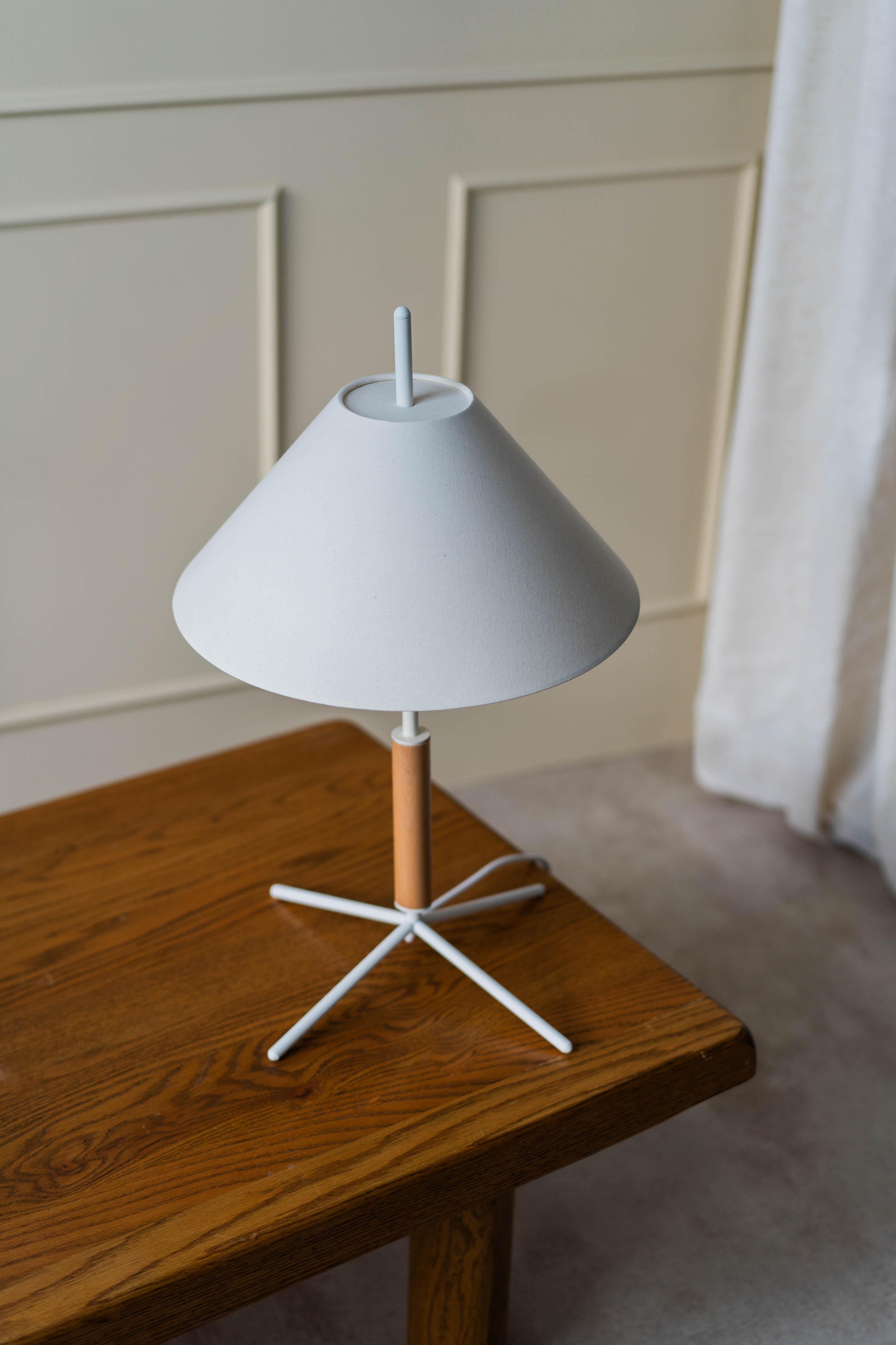 The VOL table lamp has a simple combination of lines and volumes, which create a geometric sculptural form, while being optimal in its shape for lighting spaces. 
It has a conical shade, a structure that combines metal with natural wood, and a