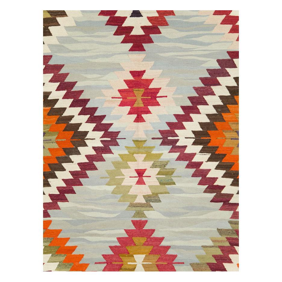 A modern Turkish flat-weave Kilim room size carpet handmade during the 21st century with a colorful geometric stepped diamond lattice pattern, often found in tribal pieces, over a blue grey background.

Measures: 9' 3