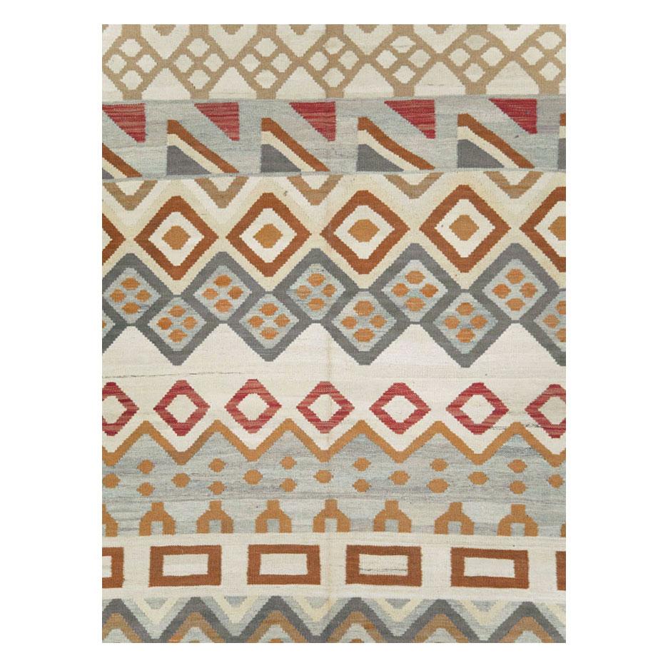 A modern Turkish flatweave Kilim room size carpet handmade during the 21st century with some tribal design elements in geometric form in shades of grey, brown, and red, over a cream background.

Measures: 9' 5
