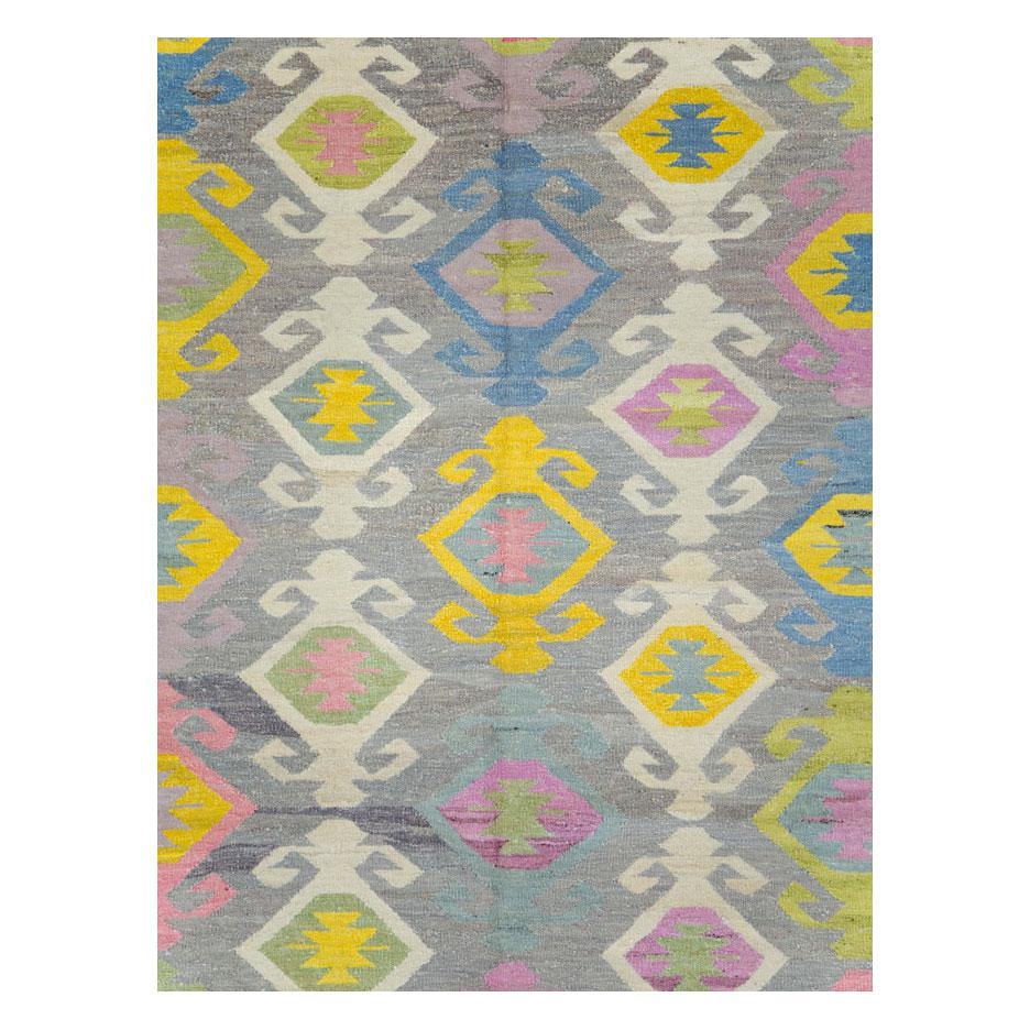 A modern Turkish Kilim flat-weave room size rug handmade during the 21st century with a grey background and light beige border. The all-over design is comprised of pastel colors including blue, yellow, pink, and green.

Measures: 10' 2