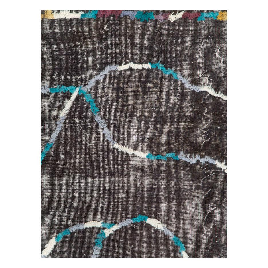 A handmade vintage Turkish Sparta rug that has been over dyed charcoal black and given a distressed appeal with hand knotted raised plush piles to form the quirky offset medallion and border of this modern folk piece.