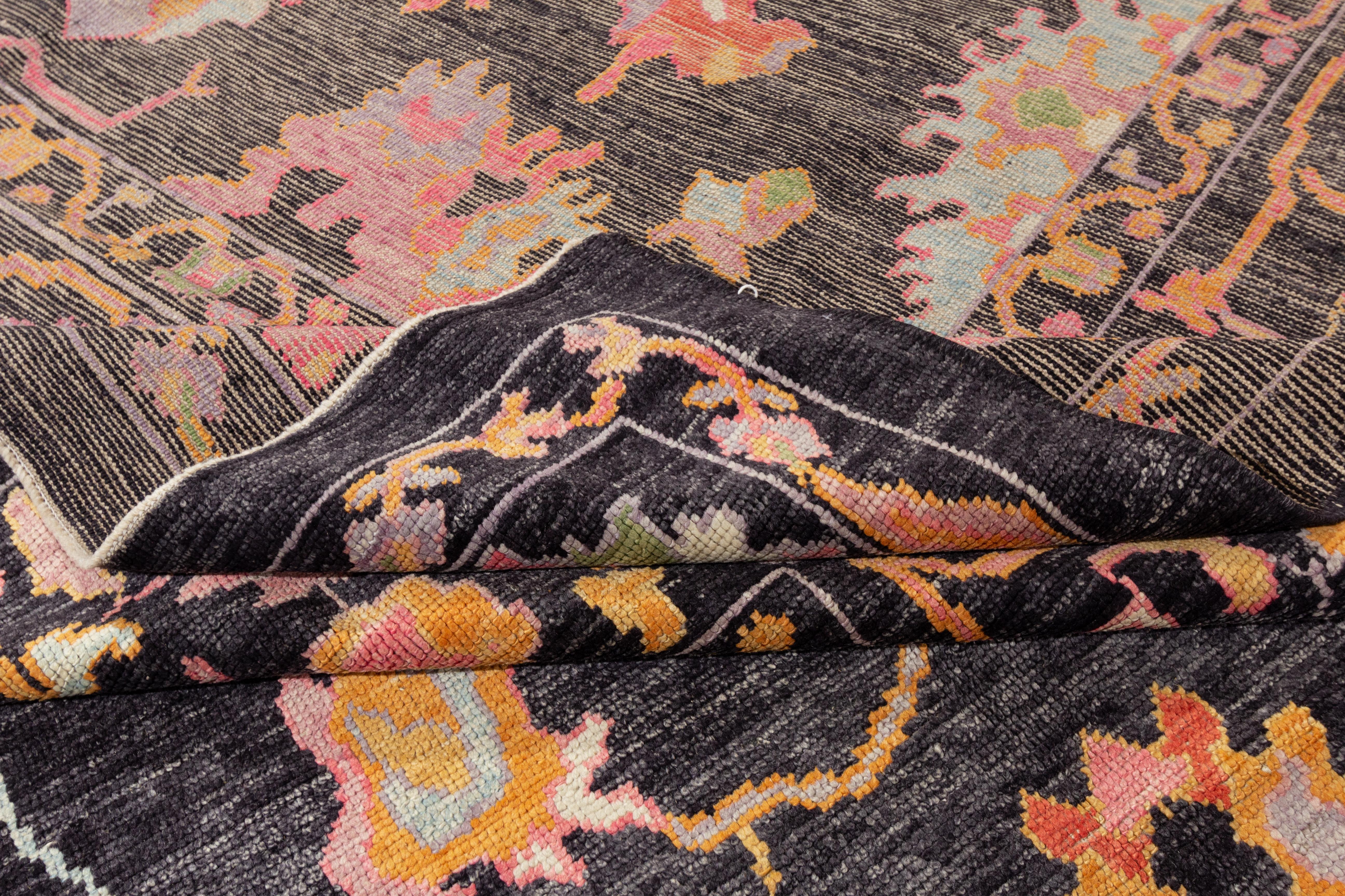 A handcrafted modern Turkish Oushak wool rug from the 21st century, featuring a charcoal field adorned with an allover floral design in shades of pink, orange, and green. 

This rug measures 10'3