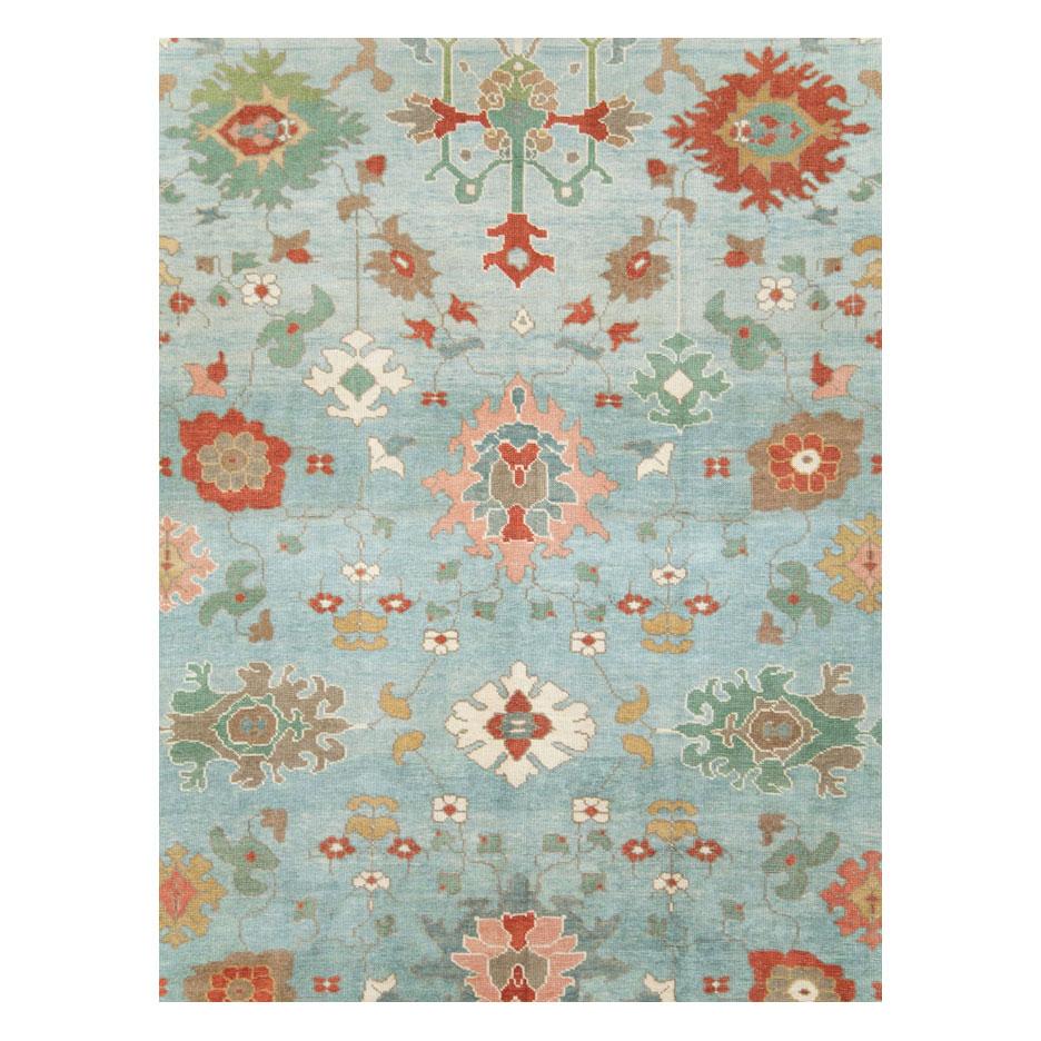 A modern Turkish Oushak room size carpet handmade during the 21st century with large palmettes in rust red and seafoam green over a lightly abrashed light blue and slate field enclosed by an ivory border.

Measures: 9' 9