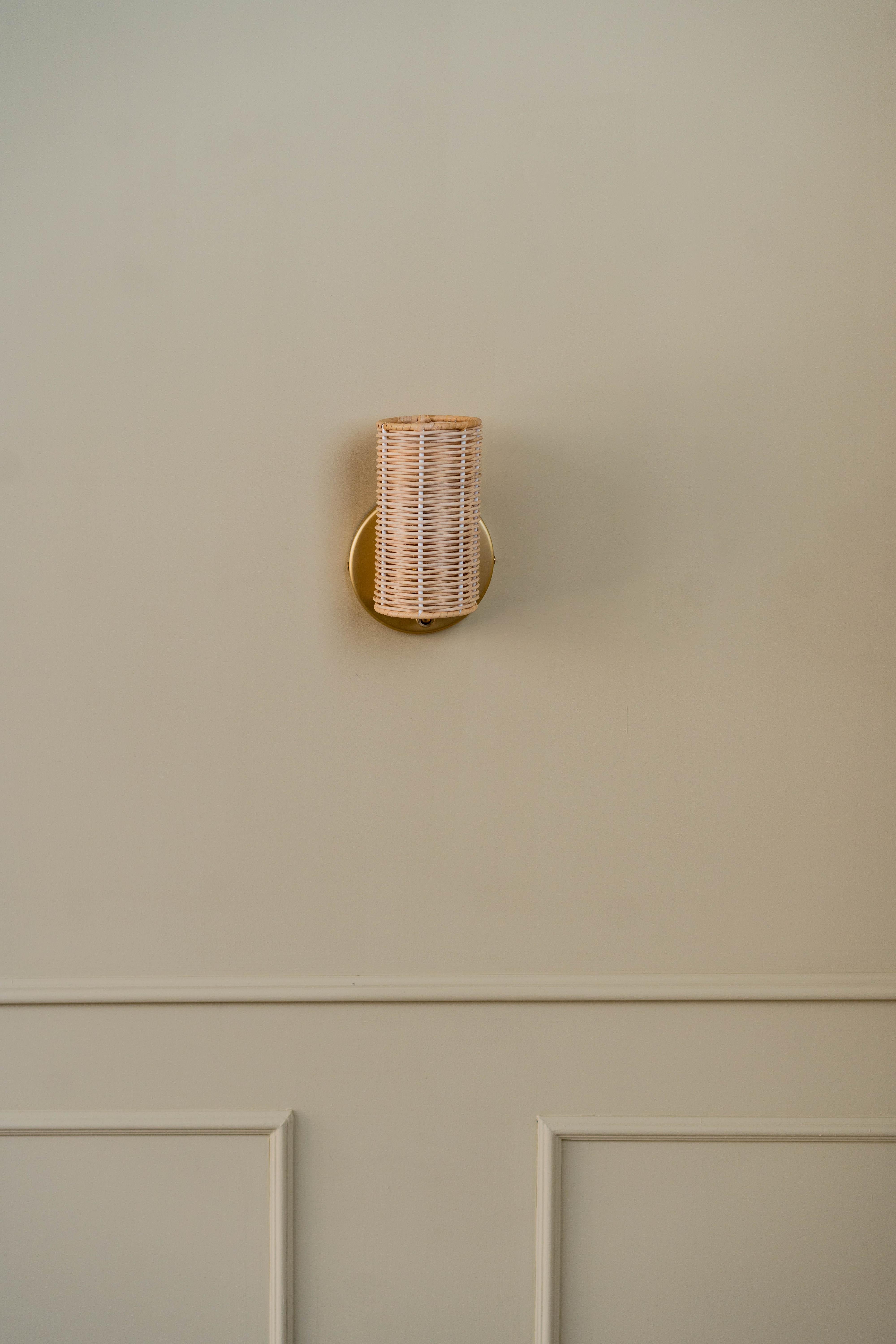 The Costa Wall Lamp Mini Rattan/Brass is a beautifully crafted piece that adds both warmth and elegance to any room. Handcrafted in Barcelona by Mediterranean Objects, this mini wall sconce is a perfect example of artisanal quality and design. The