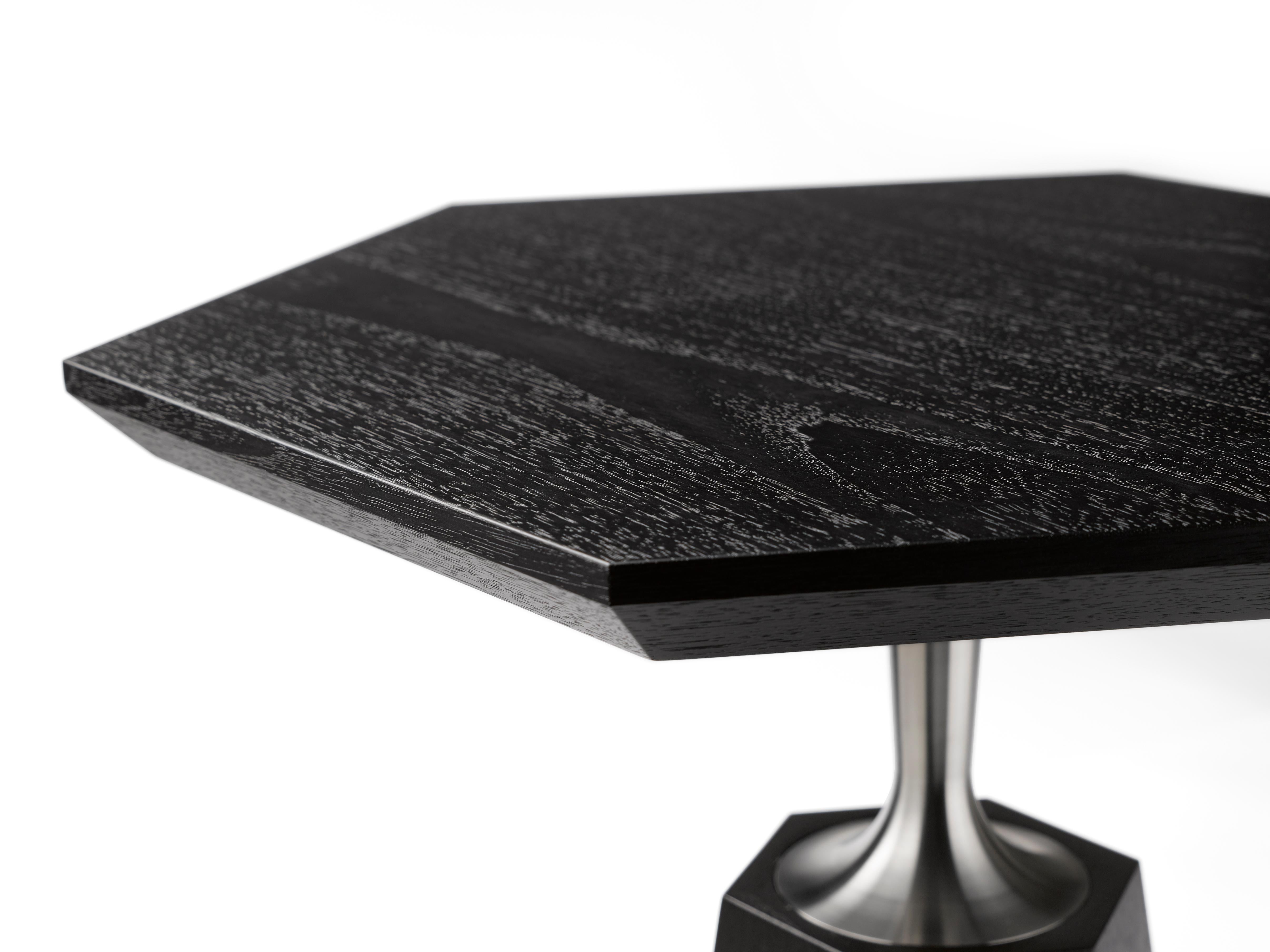 Der Hex Occasional Table hat einen sechseckigen, sich verjüngenden Sockel, der in einen präzisionsgefertigten Hals übergeht, der eine sechseckige Platte trägt, hier in schwarz lackiertem Nussbaum und maschinell gedrehtem, massivem Edelstahl.
Neben