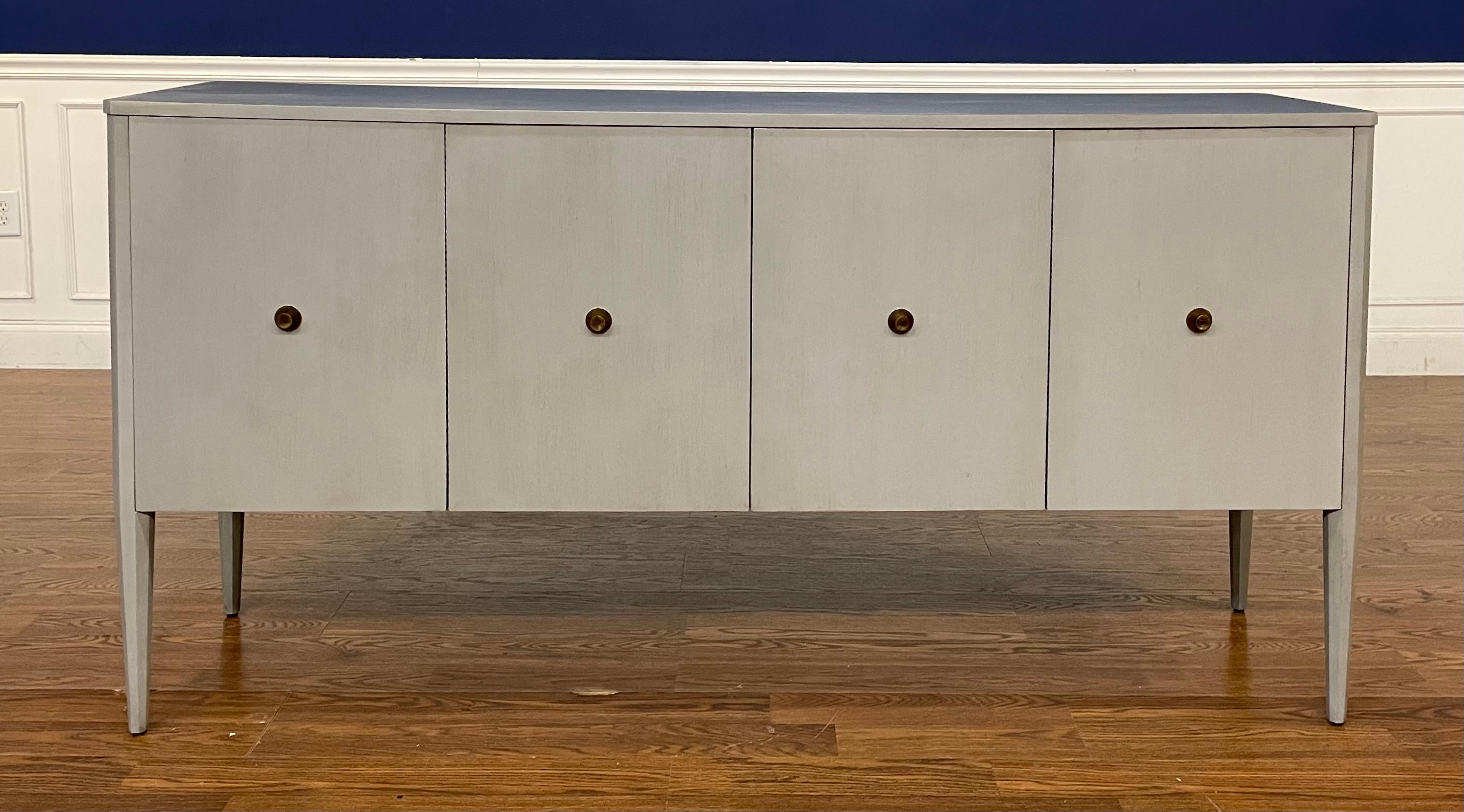 This is the Boston Sideboard by Highland House.  It features a transitional look with an artic gray color, antique brass knobs and soft-close doors.  It has adjustable shelves behind the doors. It is made with walnut veneers and beechwood solids. We