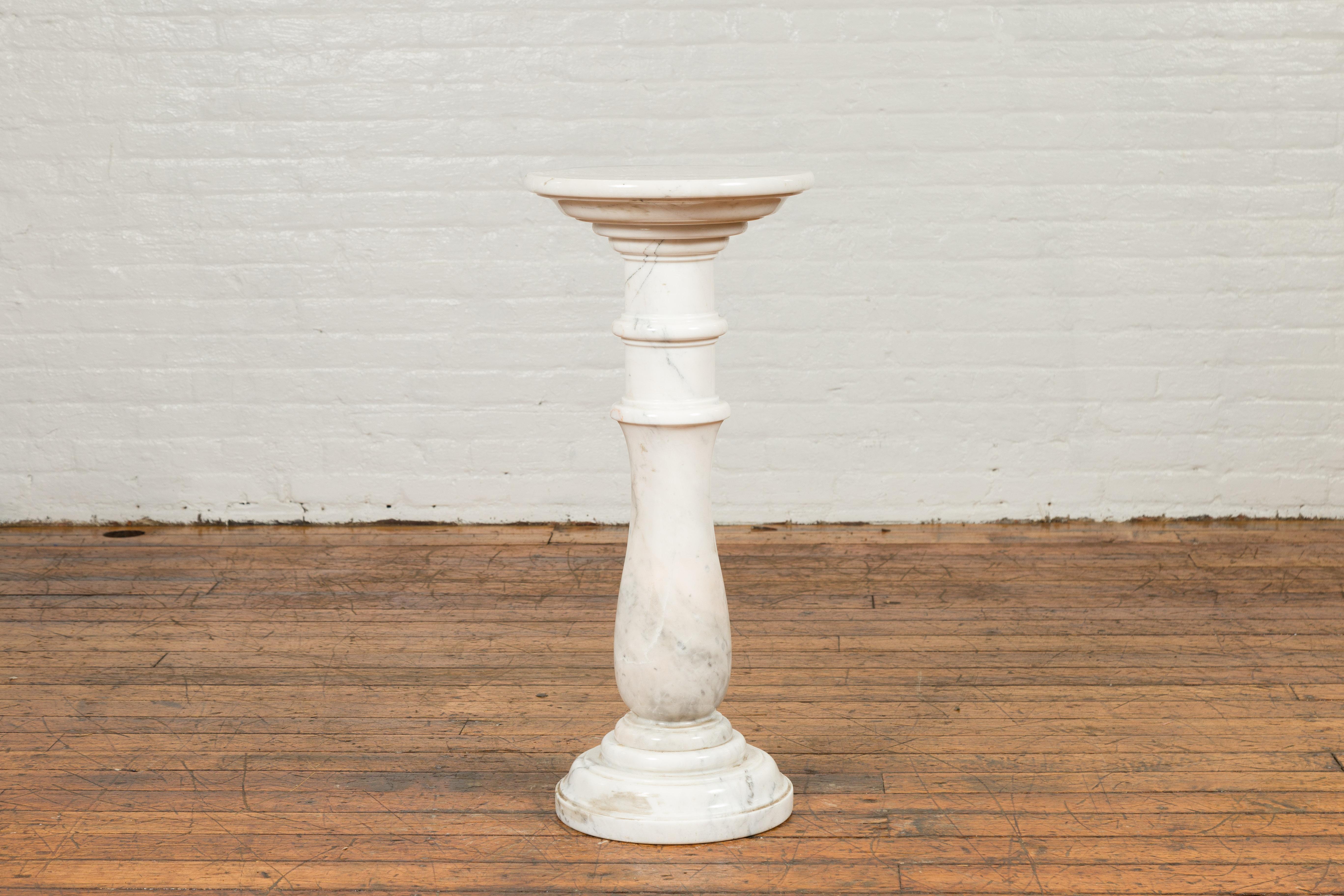 A contemporary Indian white marble pedestal with baluster base and circular top. Created in India, this marble pedestal will compliment any home decor beautifully. A circular top tapers down to rest on a baluster-shaped base, raised on a circular