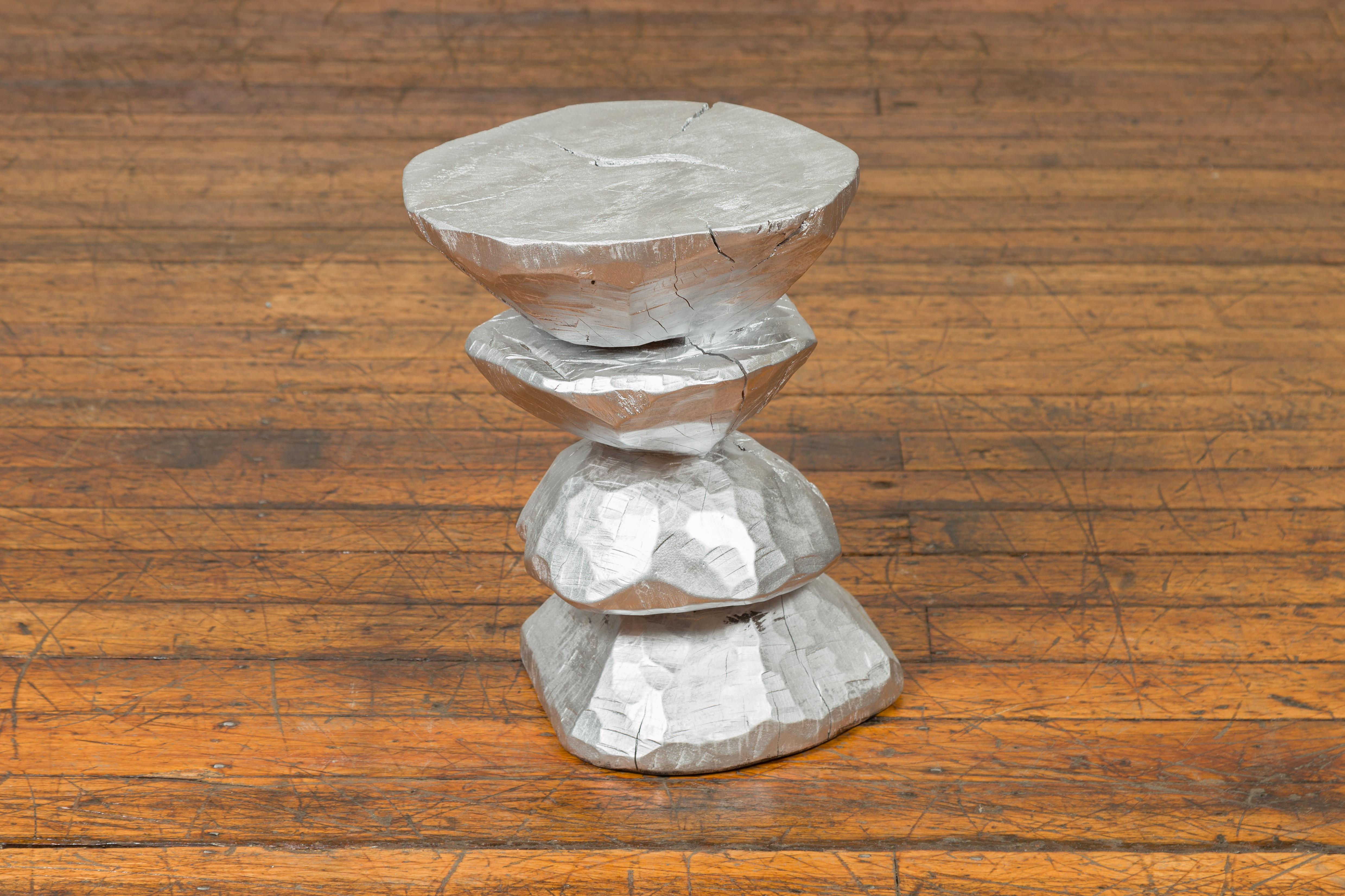 A contemporary Indonesian silver-colored wooden pedestal with tiered hourglass-inspired shape. Crafted in Indonesia, this pedestal will charm you with its shiny finish and interesting shape. Made of wood carved into irregular geometrical shapes,
