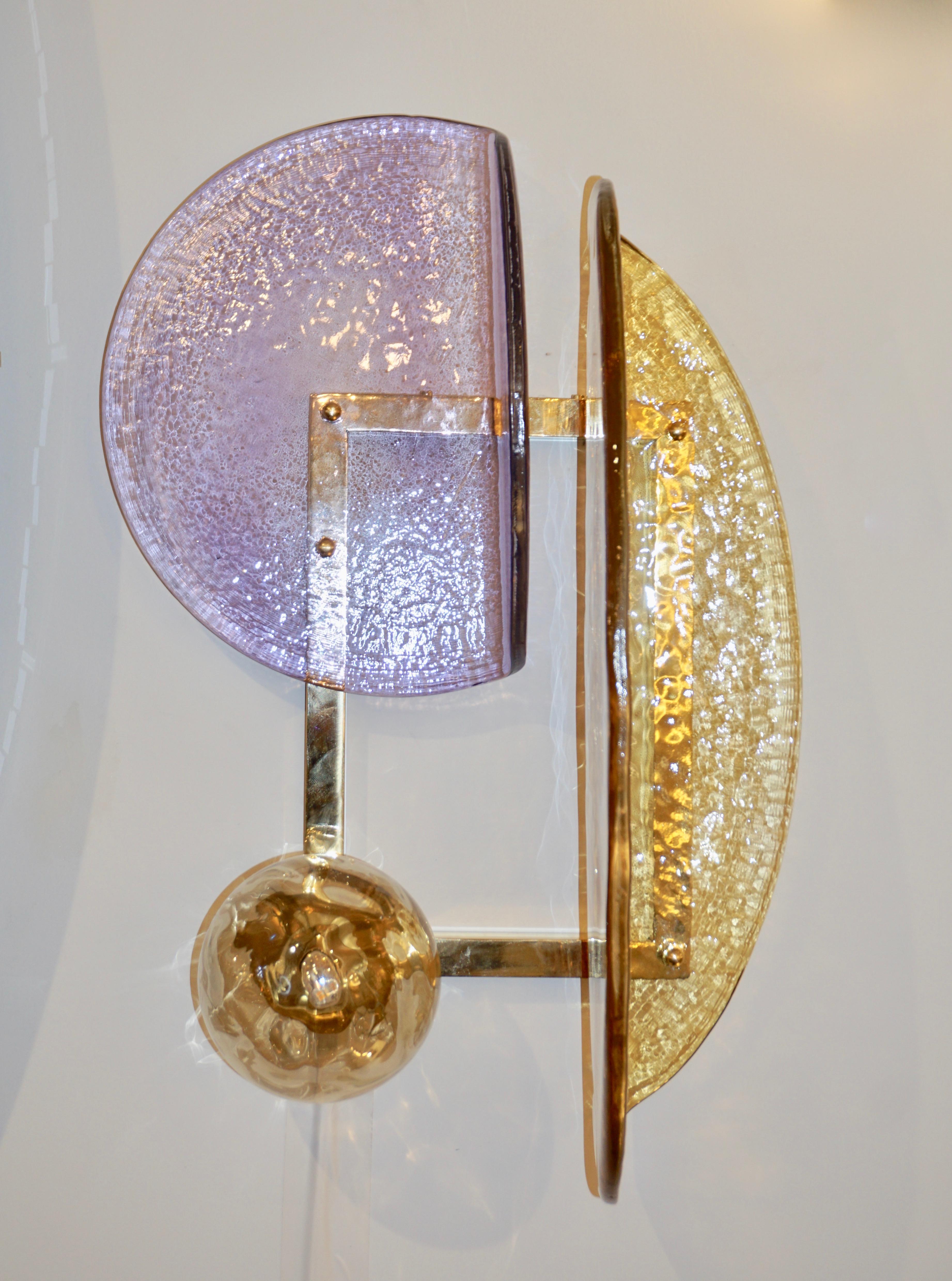 Esta lámpara de pared, una creación contemporánea con un diseño geométrico moderno y único, está fabricada totalmente a mano en Italia. Los elementos moldeados de cristal texturizado de forma curva orgánica, en cristal de Murano de color ámbar