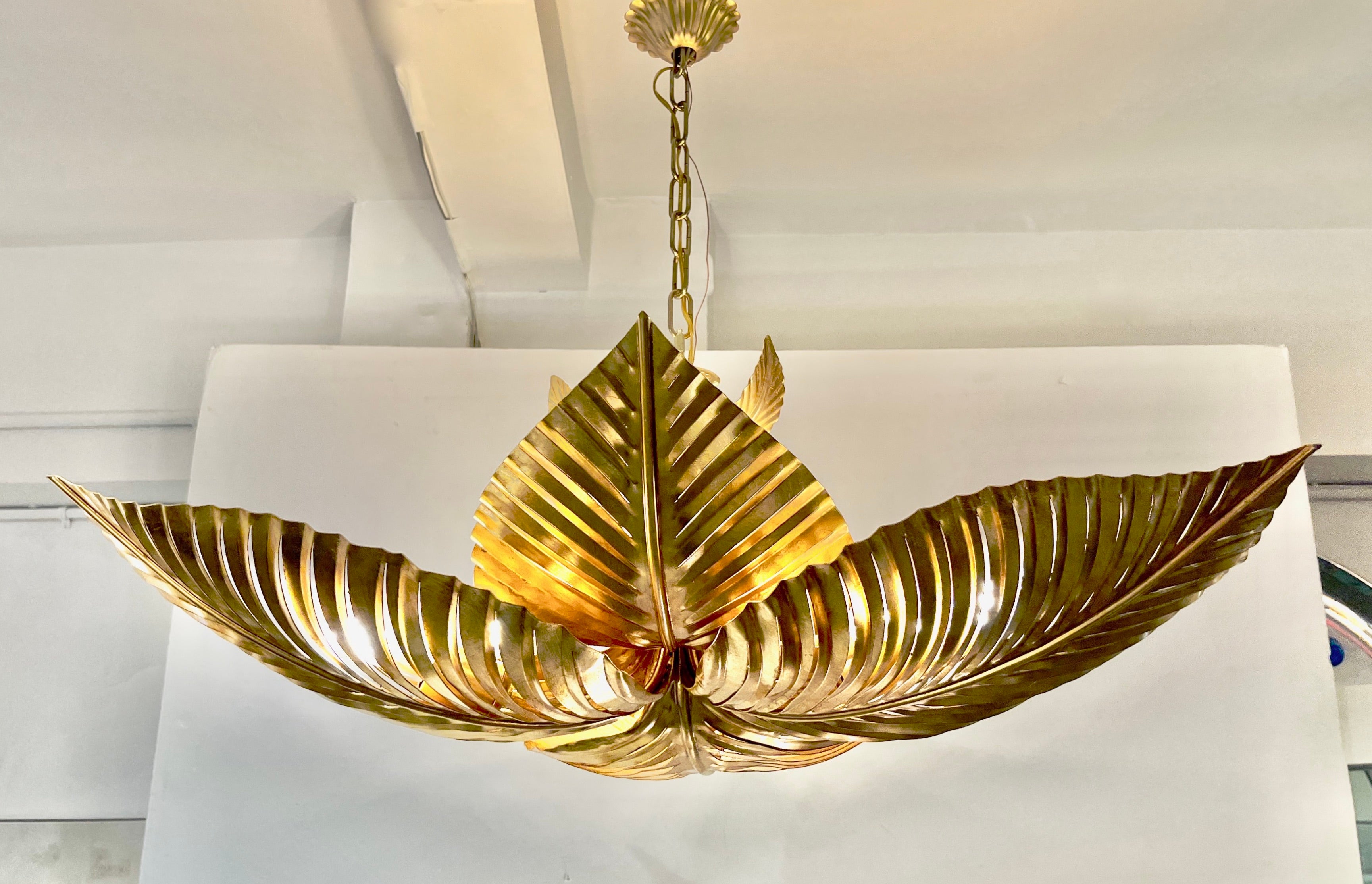 Entirely hand made in Italy, this bespoke nature inspired foliage pendant with Hollywood Regency glamour, is composed of overlapping Art Deco Design leaves made of hand-gilt iron, supported by a central stem bearing smaller leaves at the core. Each