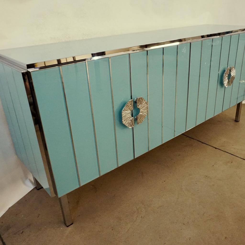 Bespoke customizable 4-door credenza/sideboard entirely handcrafted in Italy with elegant Art Deco style, the surround decorated with art glass in an enticing aquamarine pastel blue, striped with nickel inserts, raised on geometric straight nickel