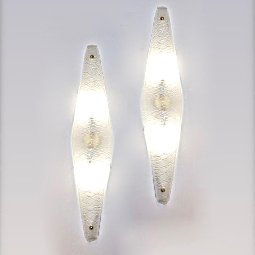 A pair of slim geometric wall lights in an unusual narrow triangle shape, entirely handcrafted in Italy, in blown frosted crystal Murano glass textured with Art Deco honeycombed pattern, on a handmade white cold painted metal frame and small brass