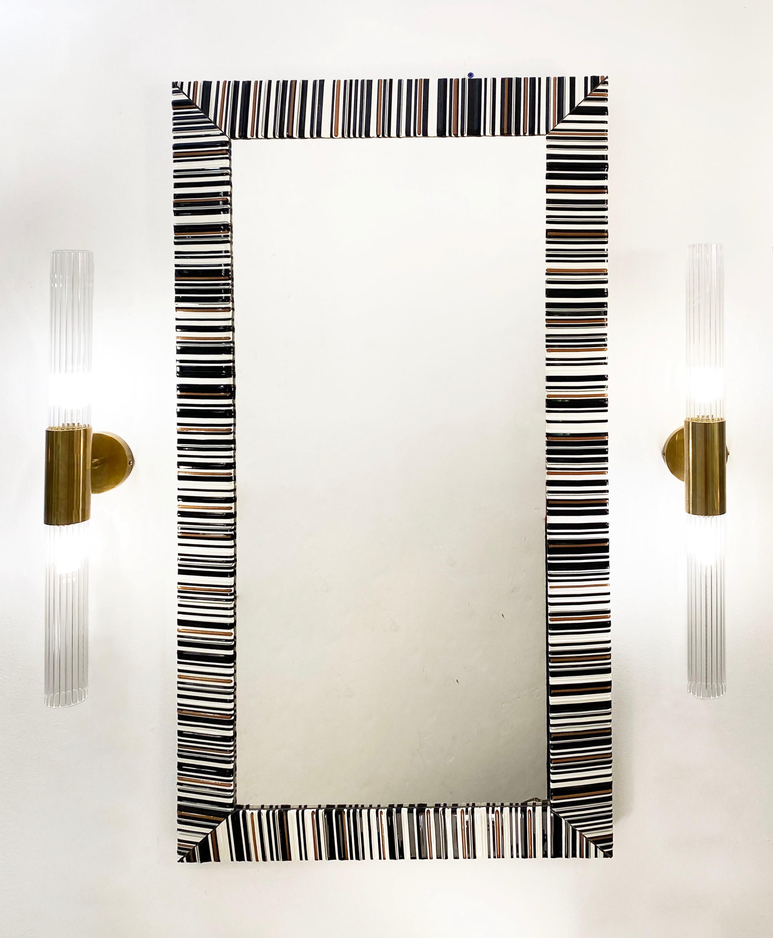 A contemporary Murano glass creation, this wall mirror is entirely handcrafted with the fusion technique in 3 glass colors: black, white, and aventurine (a difficult technique where real copper metal is mixed in the glass). Each bar is individually