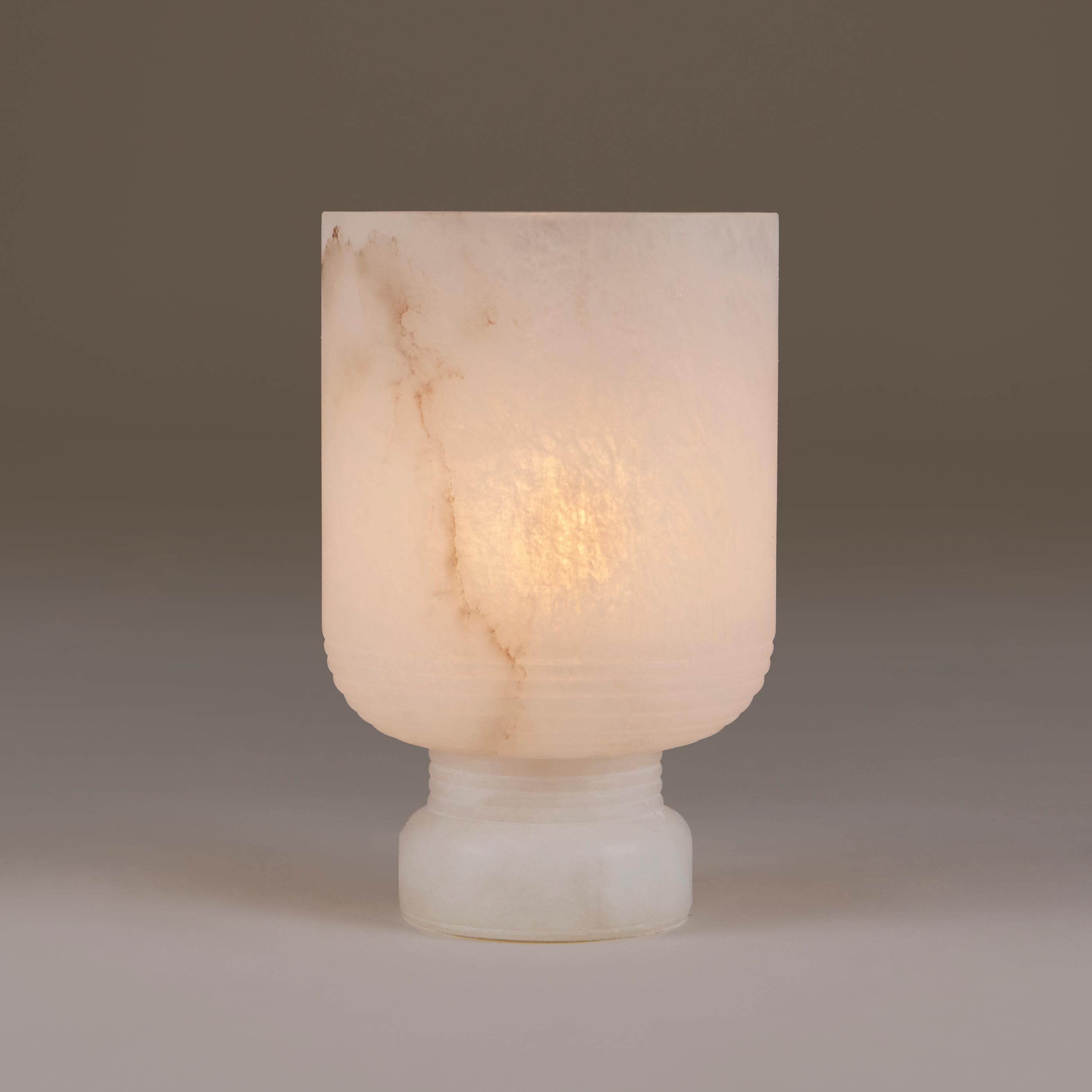 Elegantly carved base supports curved vase shaped top. The patina is enhanced by subtle markings in the alabaster and results in a soft diffused light. Each piece is made to order so variation in the marking may occur. 
Due to the handmade nature of