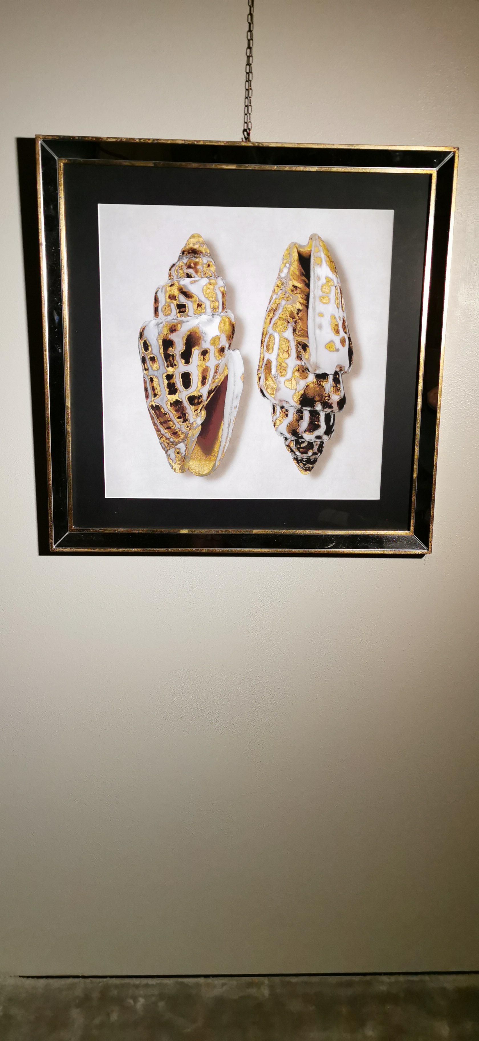 Elegante stampa colorata a mano che rappresenta due conchiglie dorate. La cornice artigianale è in legno dorato con inserti a specchio. Questa stampa è realizzata con una tecnica speciale chiamata giclée. La tecnica di stampa giclée è una