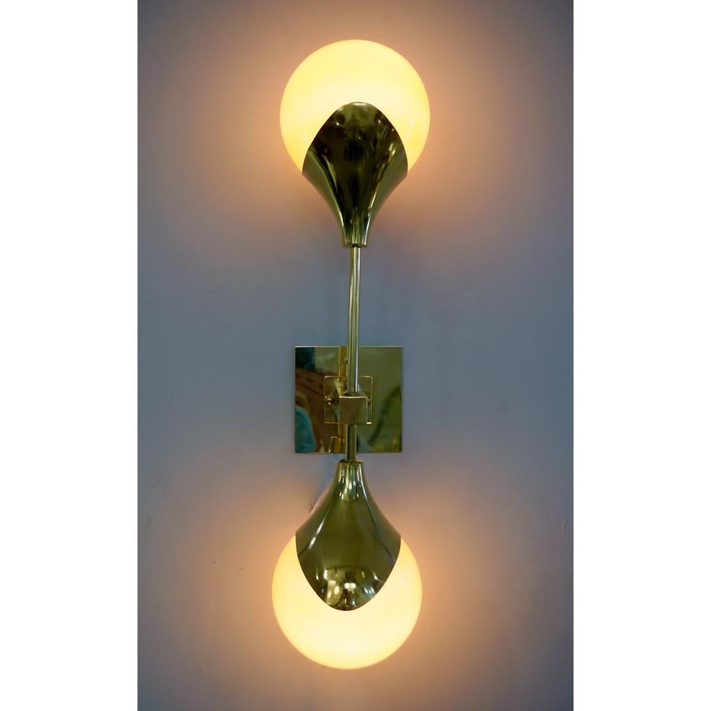 Applique contemporaine de style Stilnovo en laiton, entièrement fabriquée à la main en Italie, avec des abat-jours en verre orange qui sont recouverts de verre blanc pour produire une lumière abondante lorsqu'elle est allumée. Le bras en laiton fait