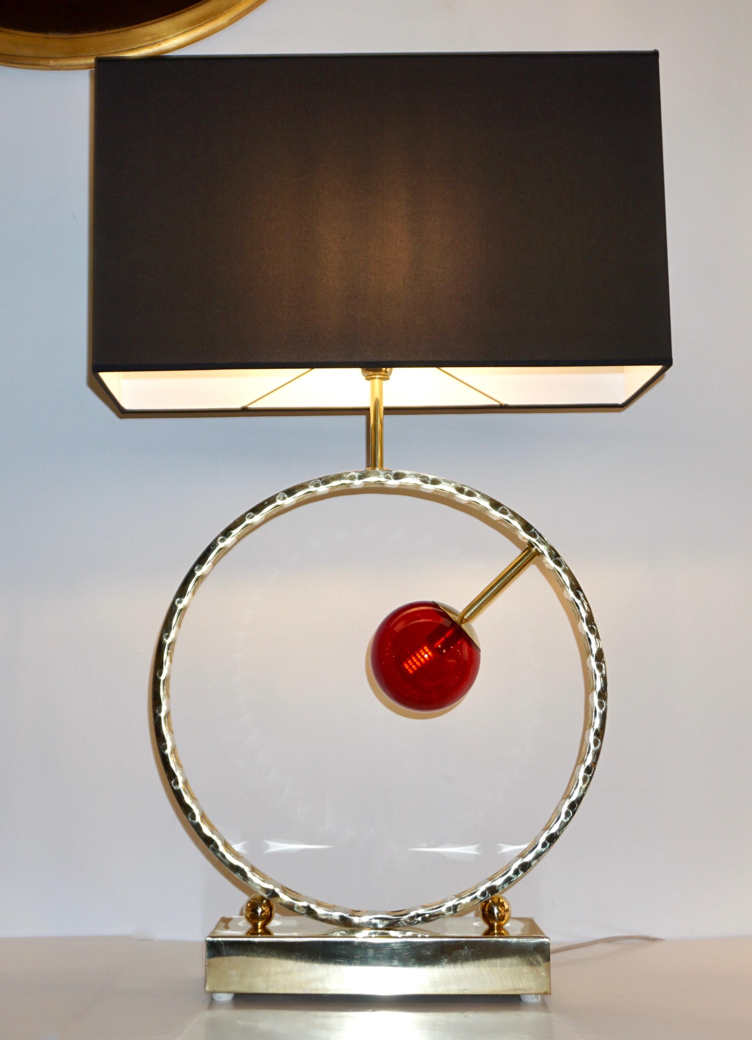 Ein Paar hochdekorative, große Tischlampen, vollständig in Italien handgefertigt, mit einem verlockenden geometrischen Design. Der Körper besteht aus einem offenen Kreis aus handgehämmertem Messing, der auf einer Seite eine Kugel aus rotem