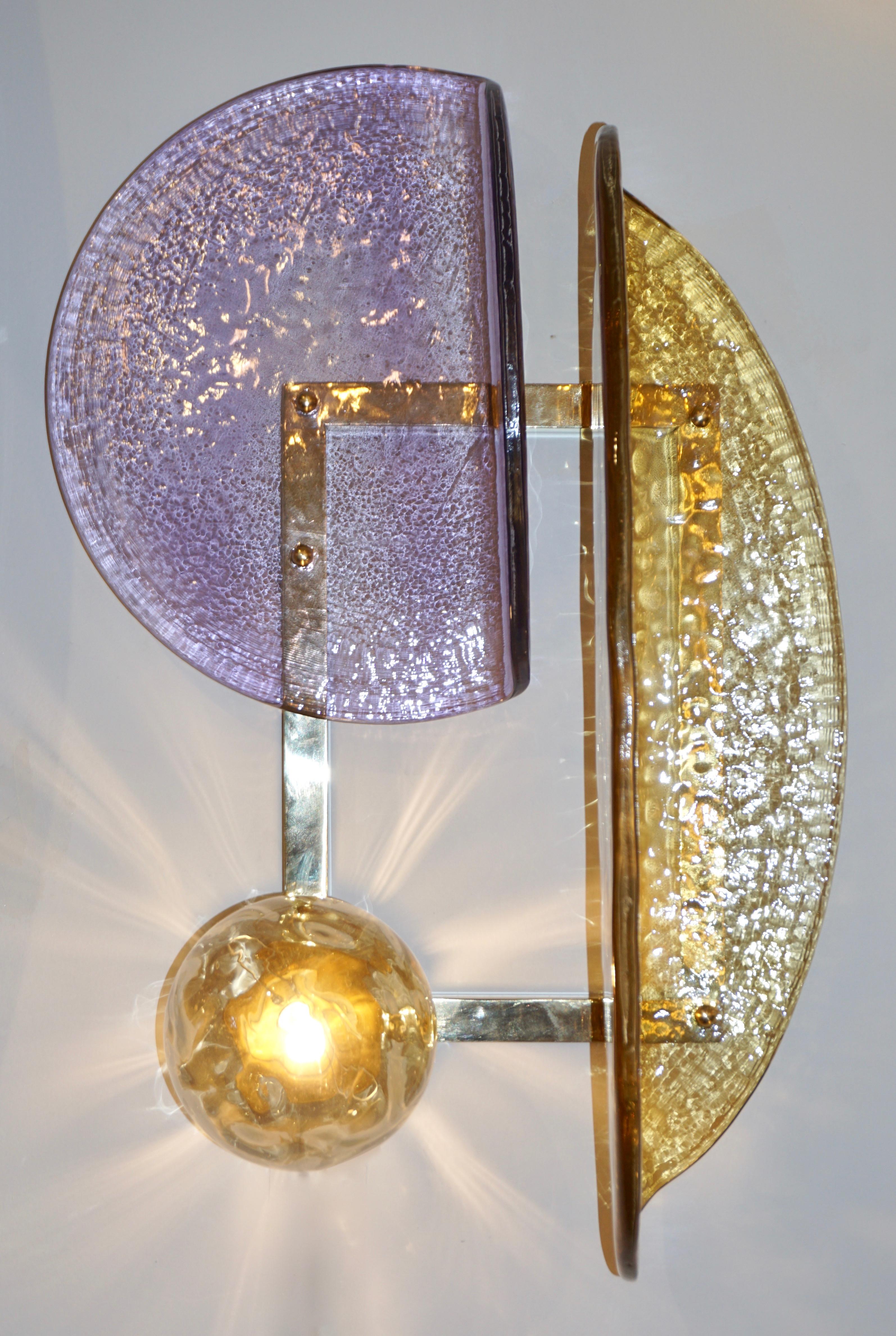 A contemporary creation with a unique modern geometric design, these wall lights are entirely handcrafted in Italy. The molded textured glass elements of organic curved shape, in amber gold and purple violet Murano glass, are mounted in a geometric
