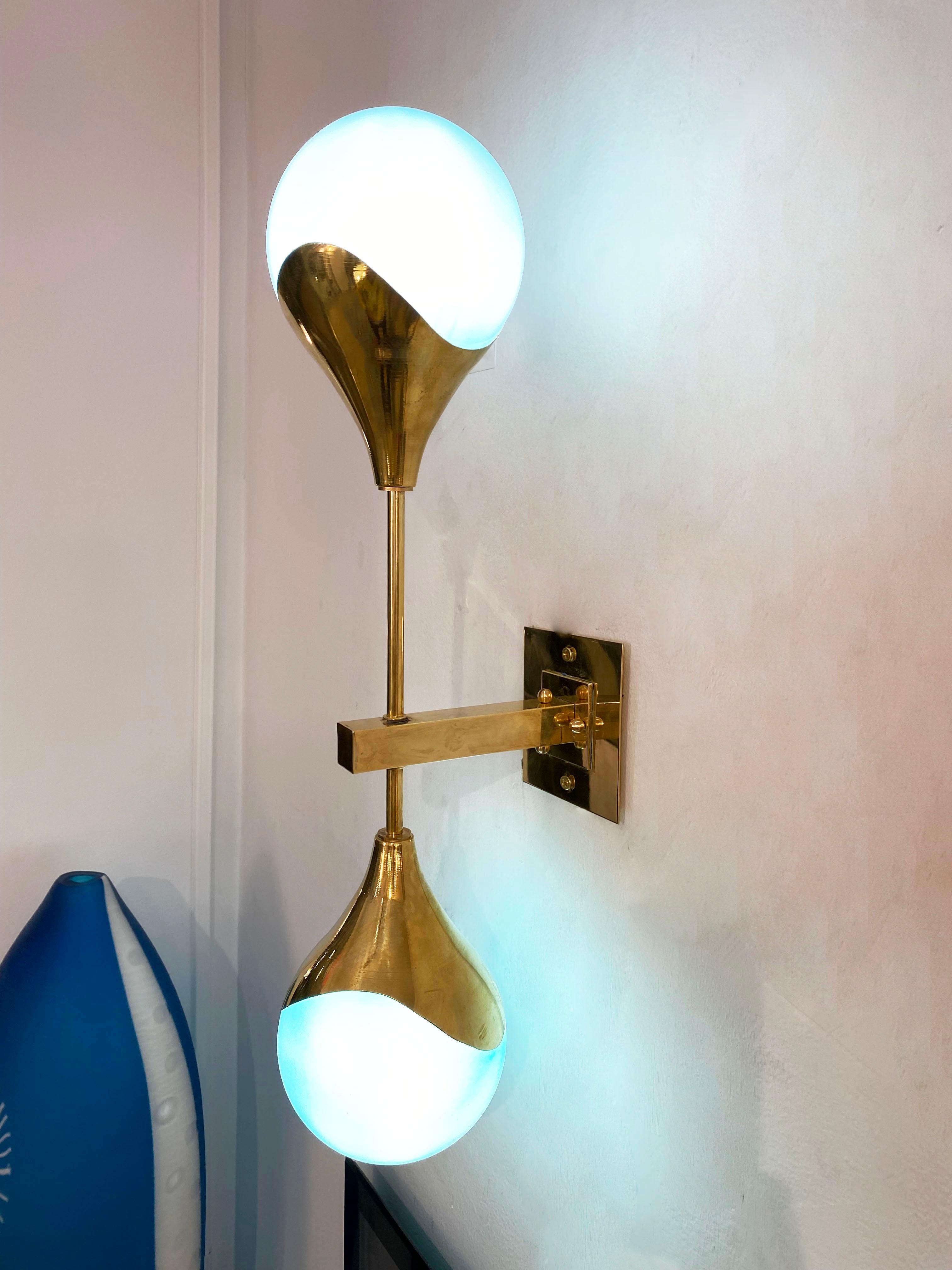 Contemporary Mid-Century Modern Stilnovo style sconces in brass, entirely handcrafted in Italy, with light blue turquoise glass shades that are overlaid in white glass to produce plenty of glowing light when lit. The handmade brass arm supports two