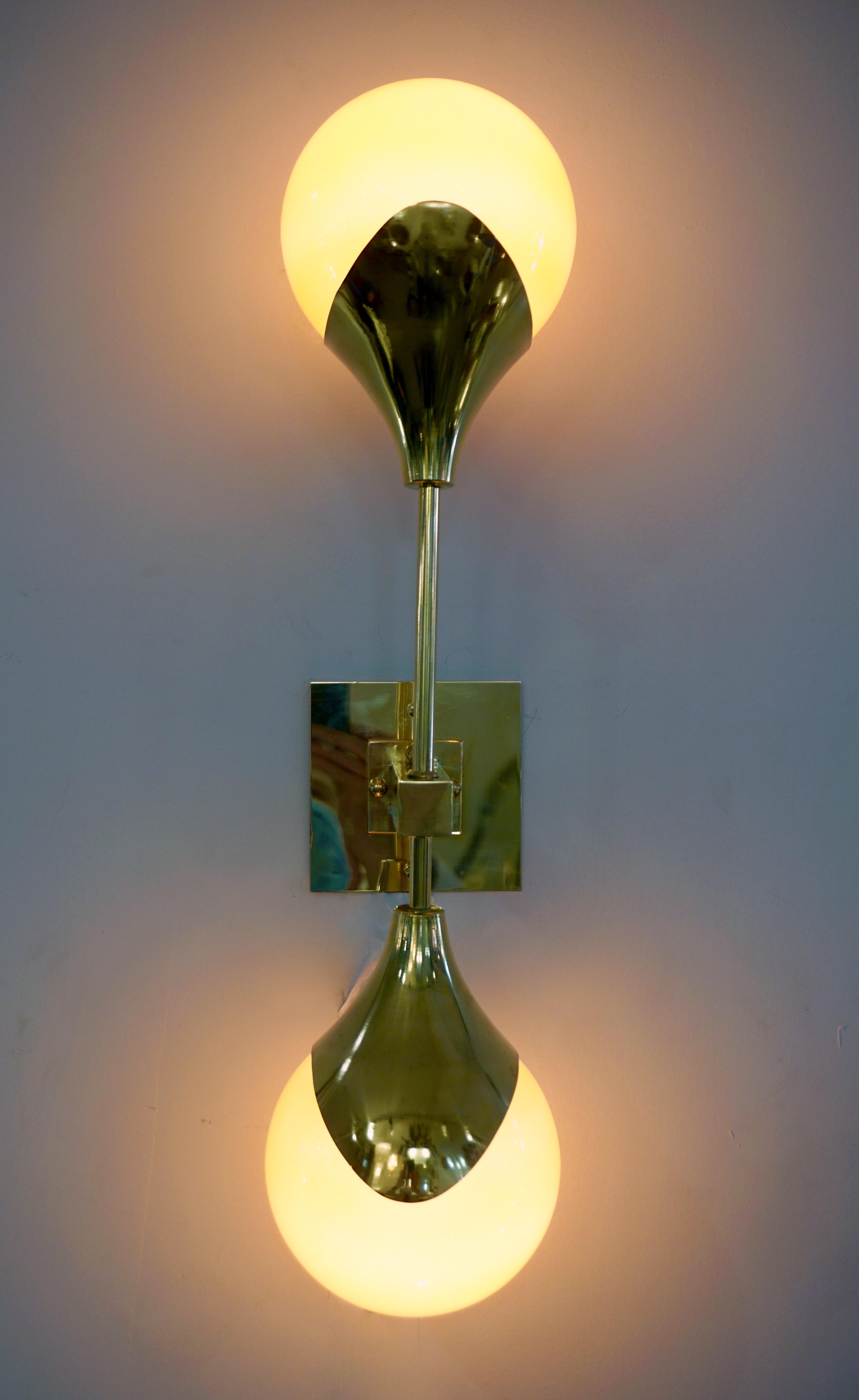 Contemporary Mid-Century Modern Stilnovo style sconce in brass, entirely handcrafted in Italy, with orange glass shades that are overlaid in white glass to produce plenty of glowing light when lit. The handmade brass arm supports two vertical poles