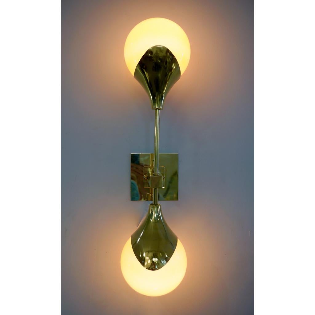 Contemporary Mid-Century Modern Stilnovo style sconce in brass, entirely handcrafted in Italy, with orange glass shades that are overlaid in white glass to produce plenty of glowing light when lit. The handmade brass arm supports two vertical poles