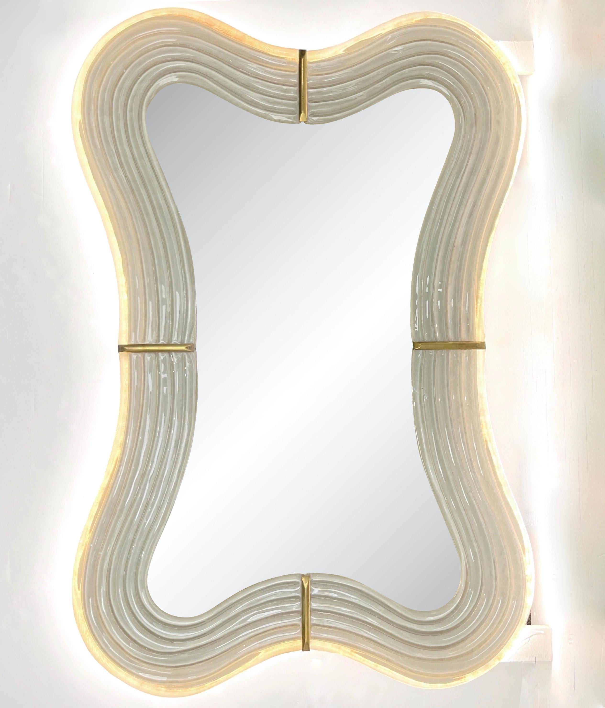 This Venetian mirror brings a sensuous soothing feeling with its curved silhouette, entirely handcrafted in Italy. The sexy waved shape presents exquisite craftsmanship: the wood backed frame, entirely edged in brass, is decorated with a reeded