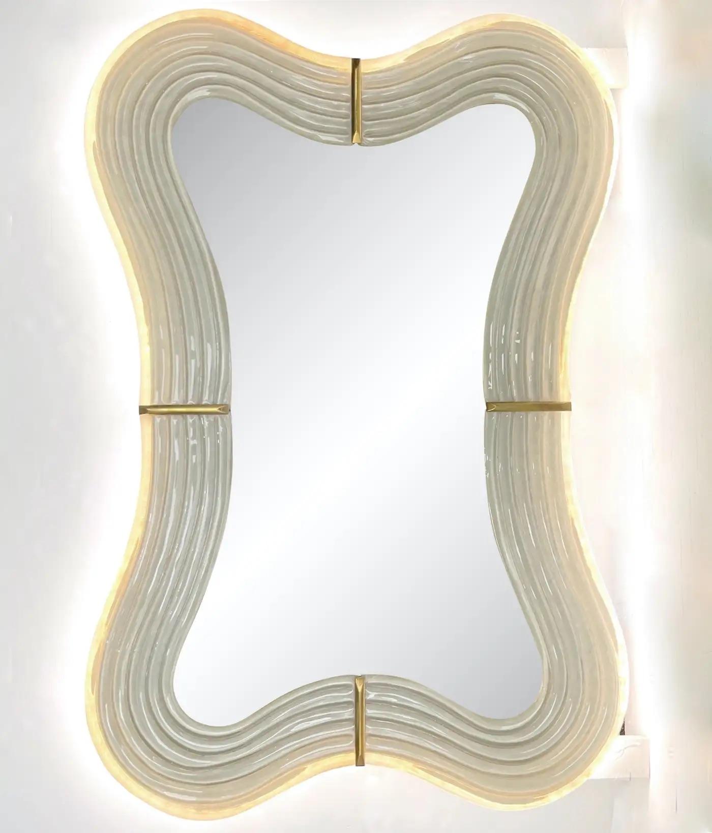 This Venetian mirror brings a sensuous soothing feeling with its curved silhouette, entirely handcrafted in Italy. The sexy waved shape presents exquisite craftsmanship: the wood backed frame, entirely edged in brass, is decorated with a reeded