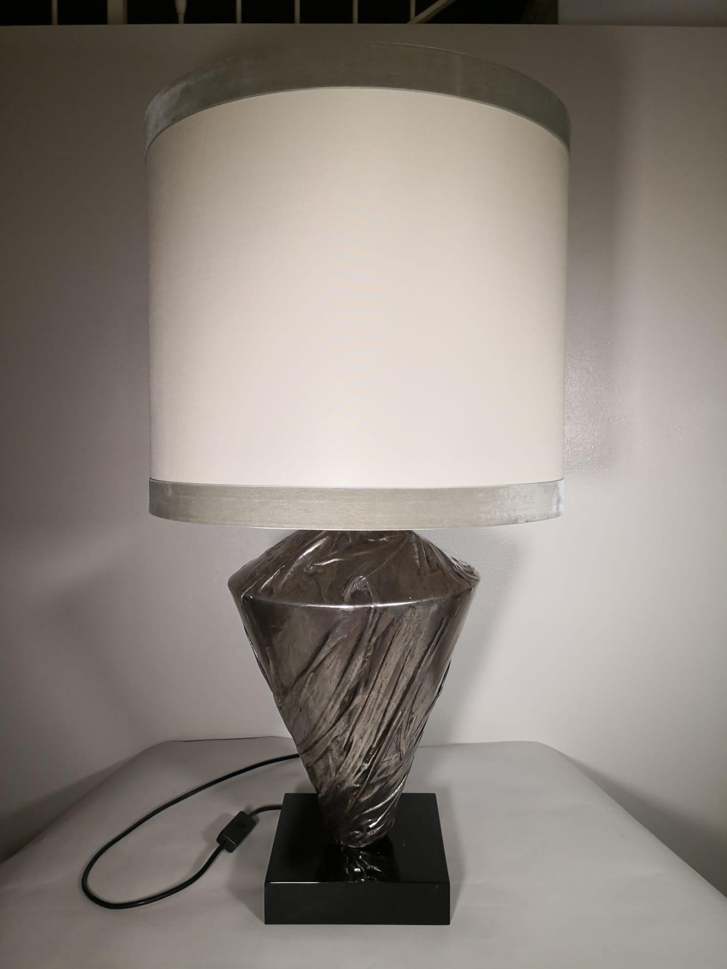 This is a very unique lamp, completely hand decorated through a very articulate process. 

Its wooden body is covered with high heat plastered tissue. This tissue is then silver plated with silver burnished leaves that are applied by using Agata